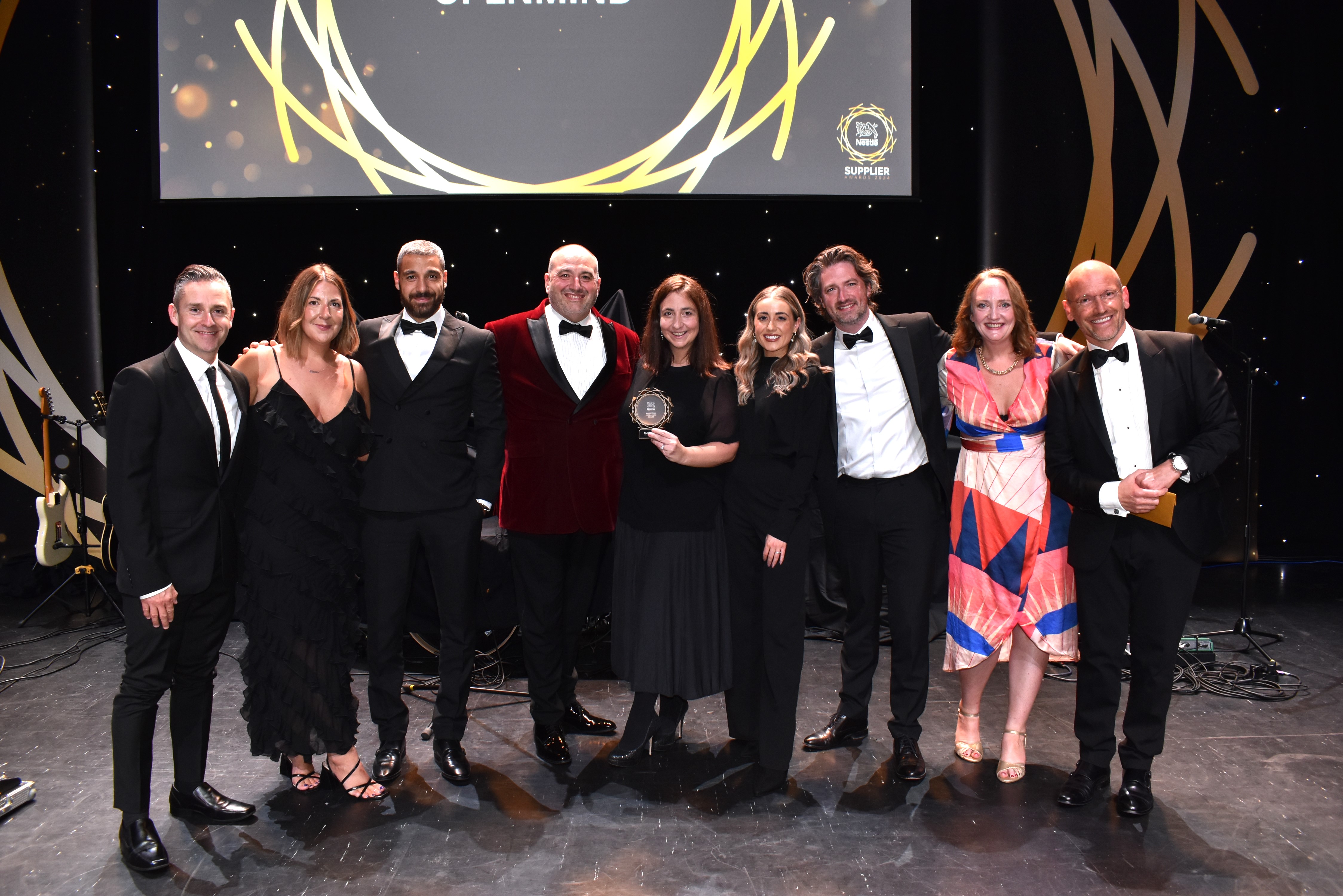 Nine people standing on a stage surrounding an award.