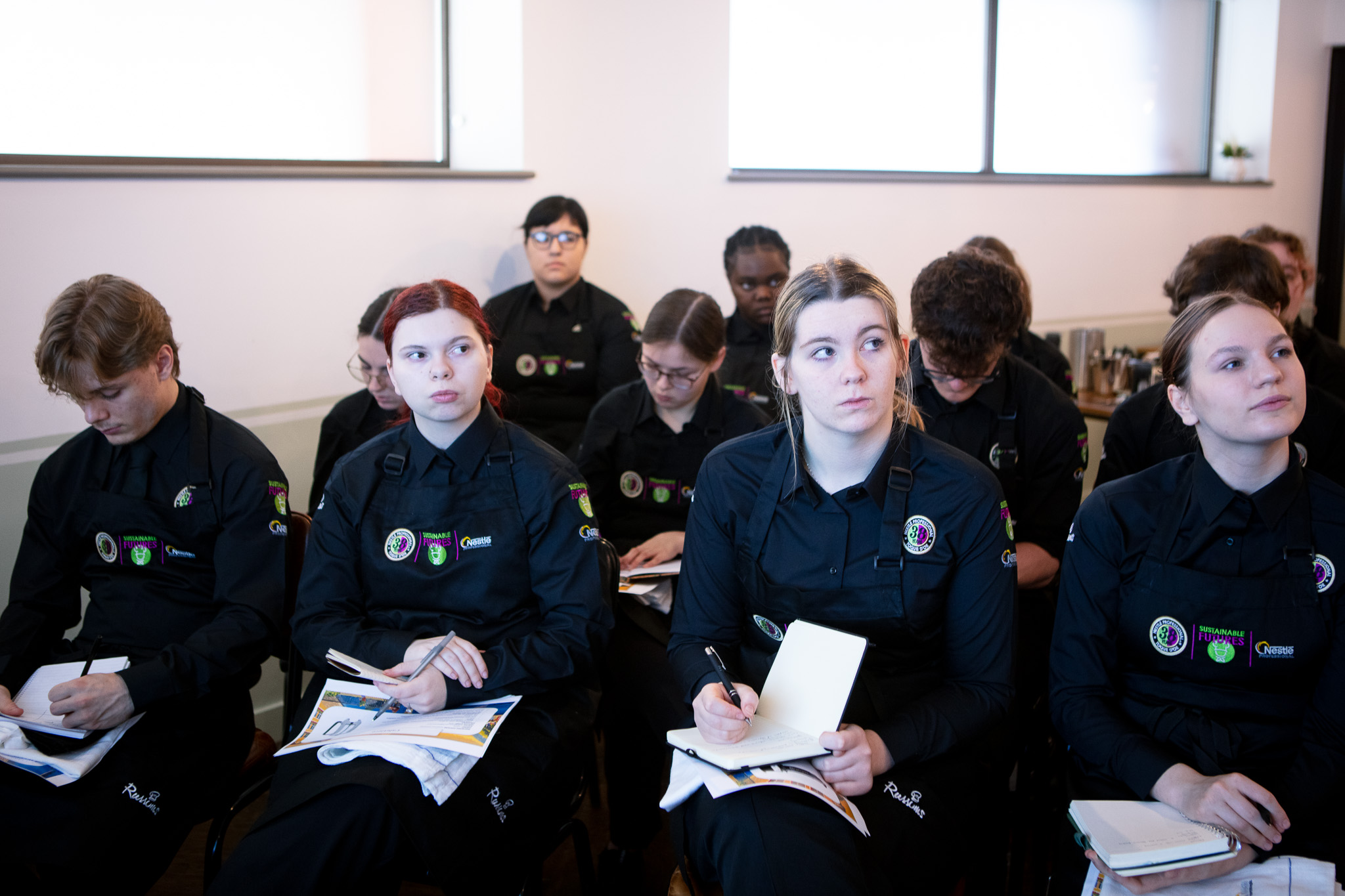 A landscape image of a group of young Toque d'Or contestants taking notes during the finals of the competition.