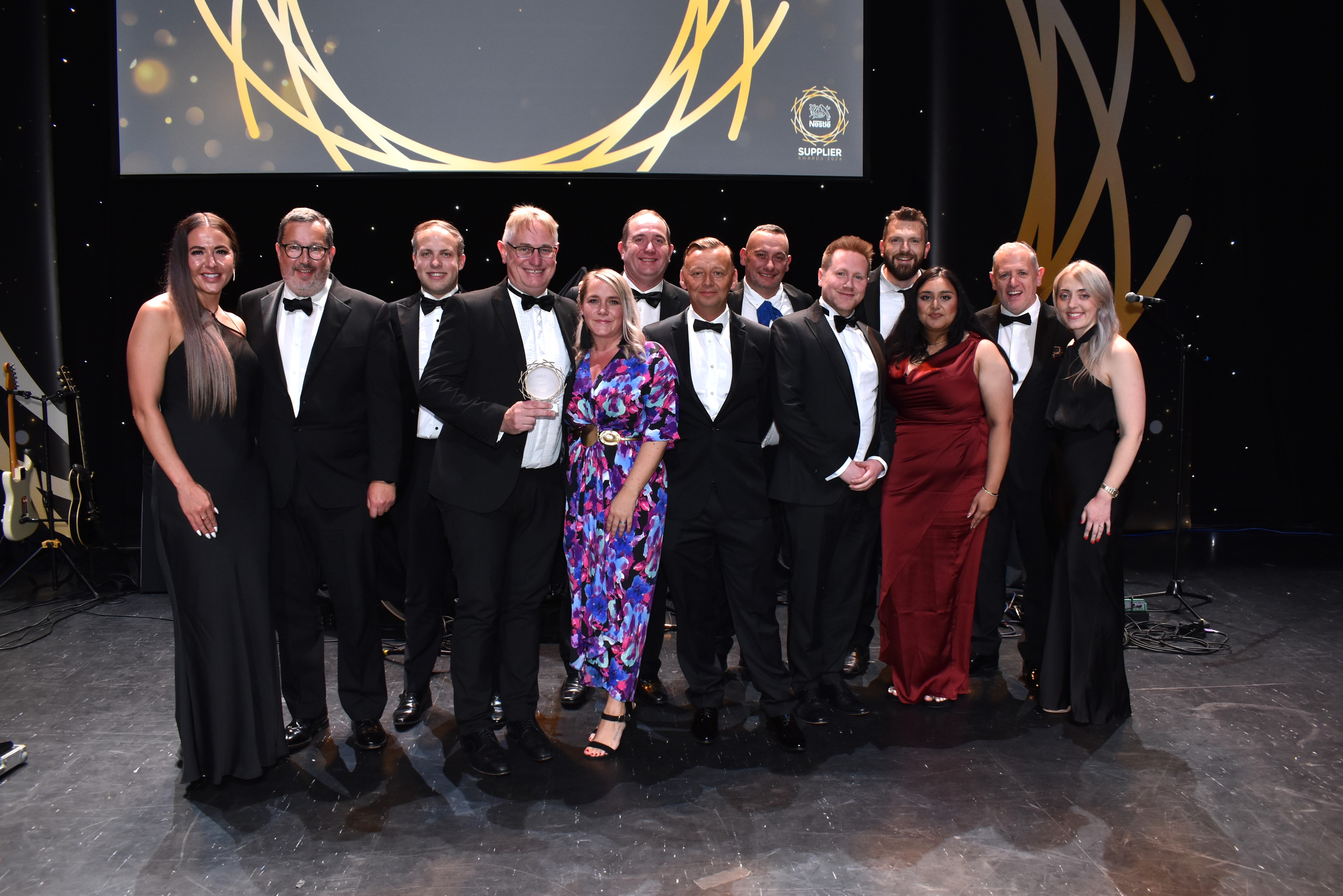 Thirteen people standing on stage and surrounding an award.