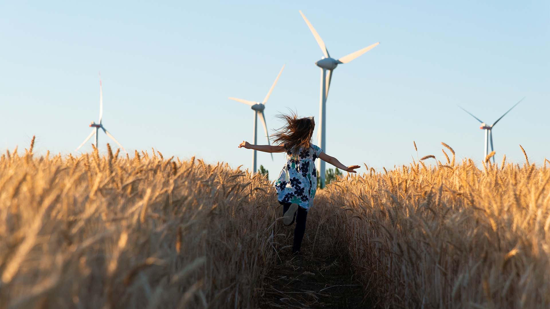 Girl running field wind turbine
