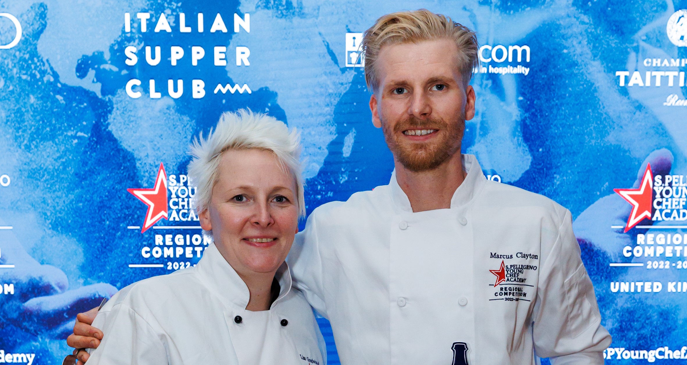 A woman and a man, who is holding an award, in chef jackets standing in front of a blue background. 