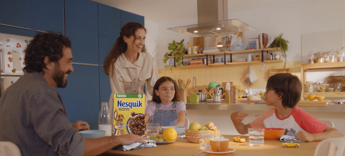A mother and father sitting with their daughter and son, each eating a bowl of Nesquik at the kitchen table.