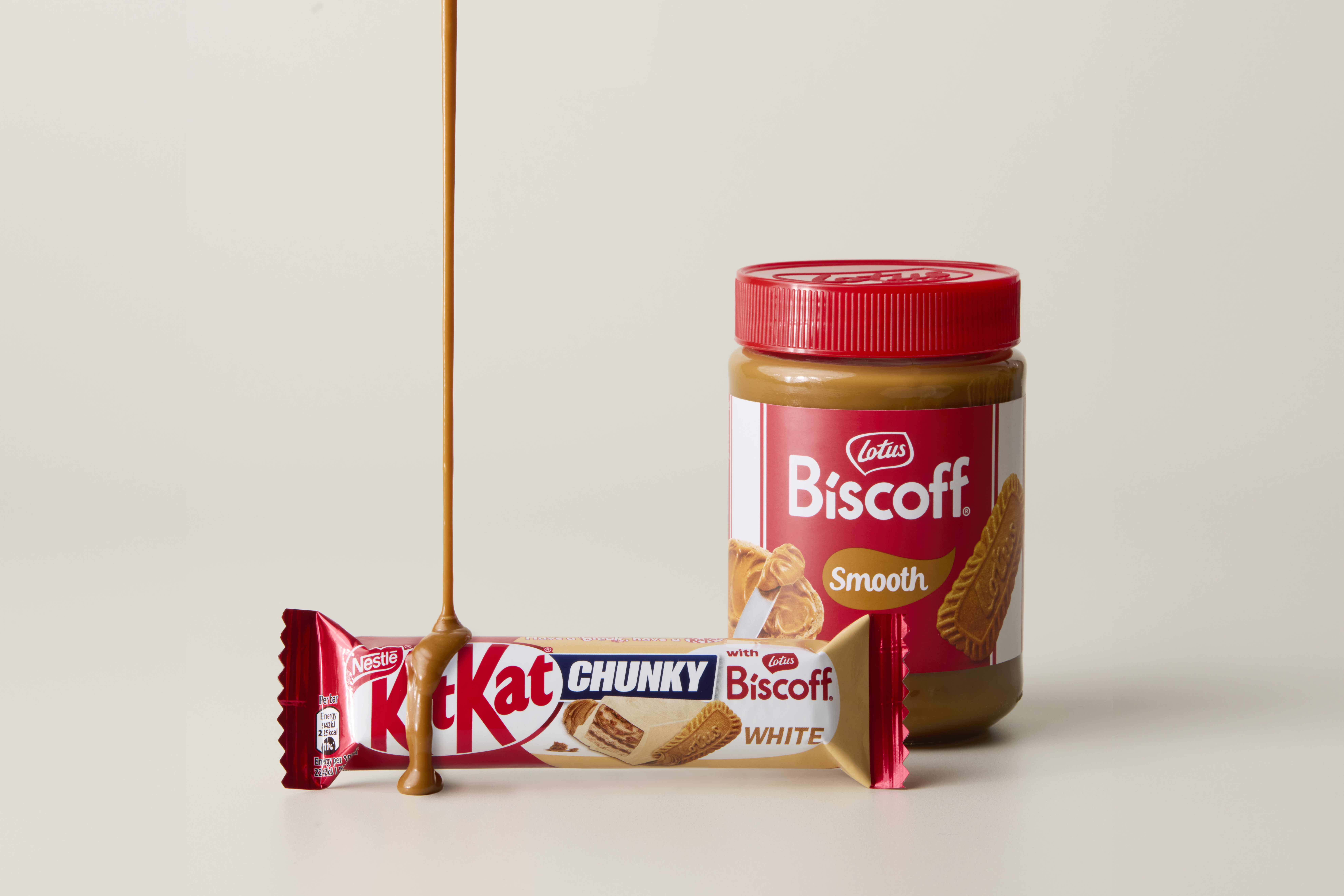 Jar of Lotus Biscoff next to a KitKat Chunky bar. Smooth and melted Lotus Biscoff is dripping onto the KitKat Chunky.