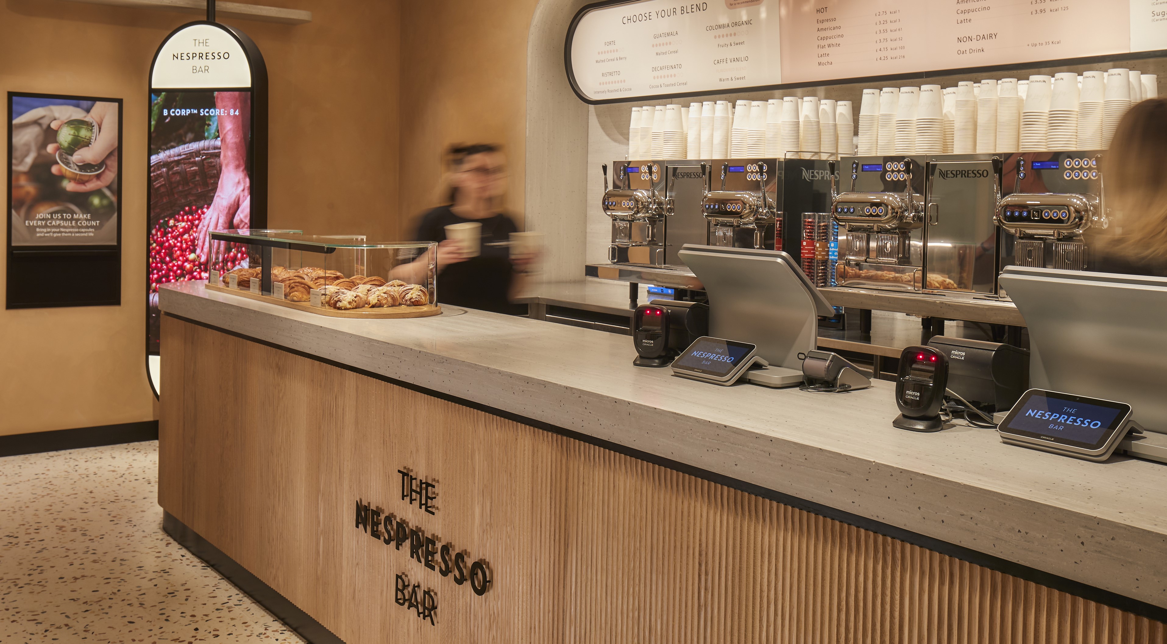 A wooden brown cafe bar with coffee machines and pastries on the counter top. 