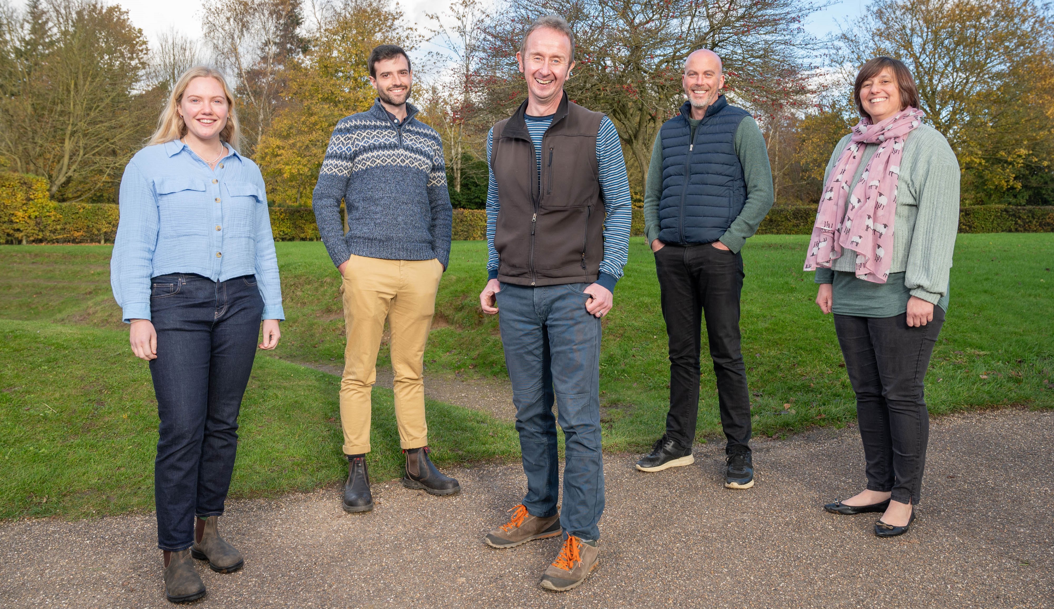 group of five people standing in a park, smiling at the camera