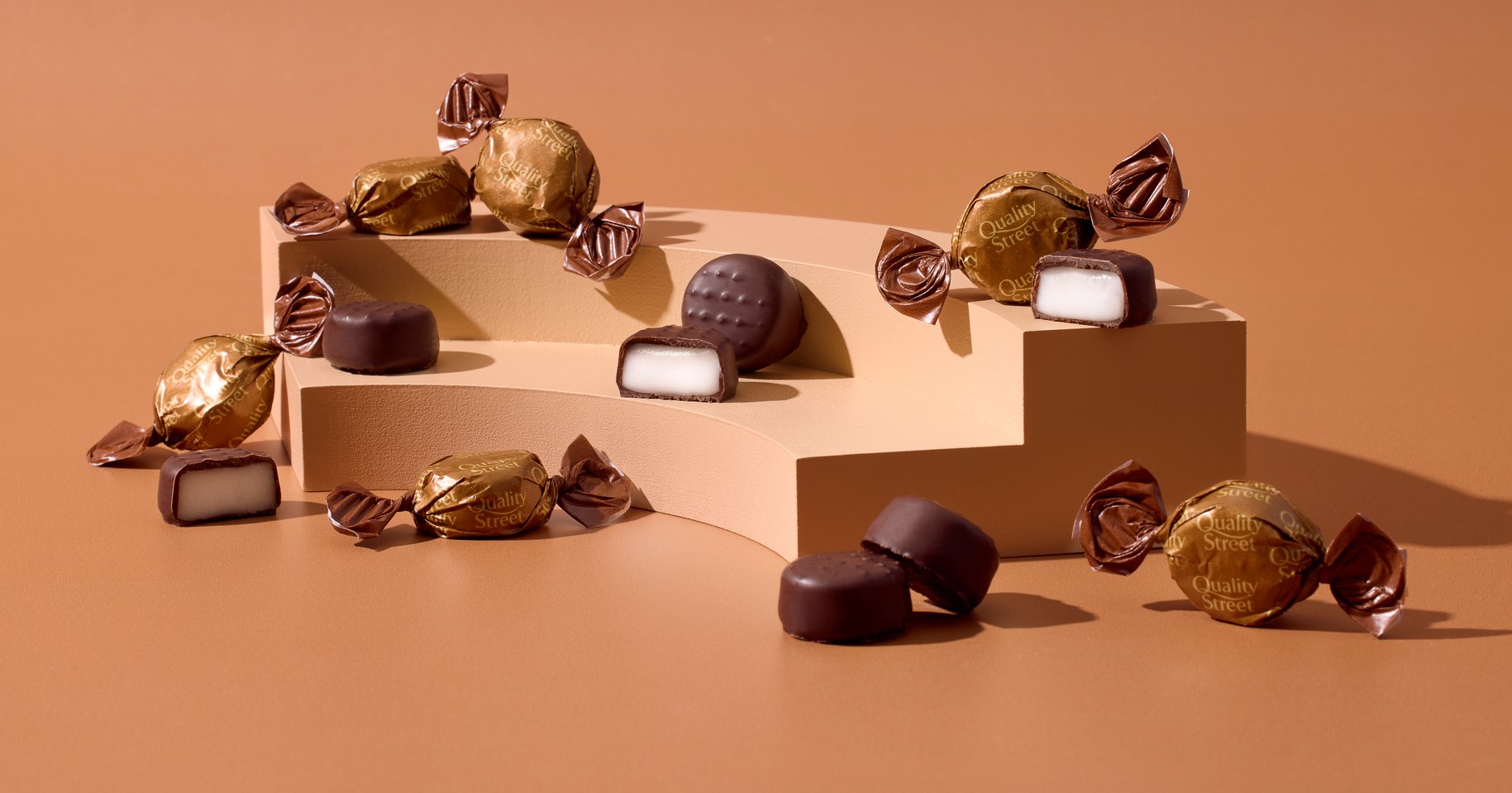 A selection of coffee creme sweets wrapped in a golden brown twist wrap next to unwrapped coffee creme with a white centre.