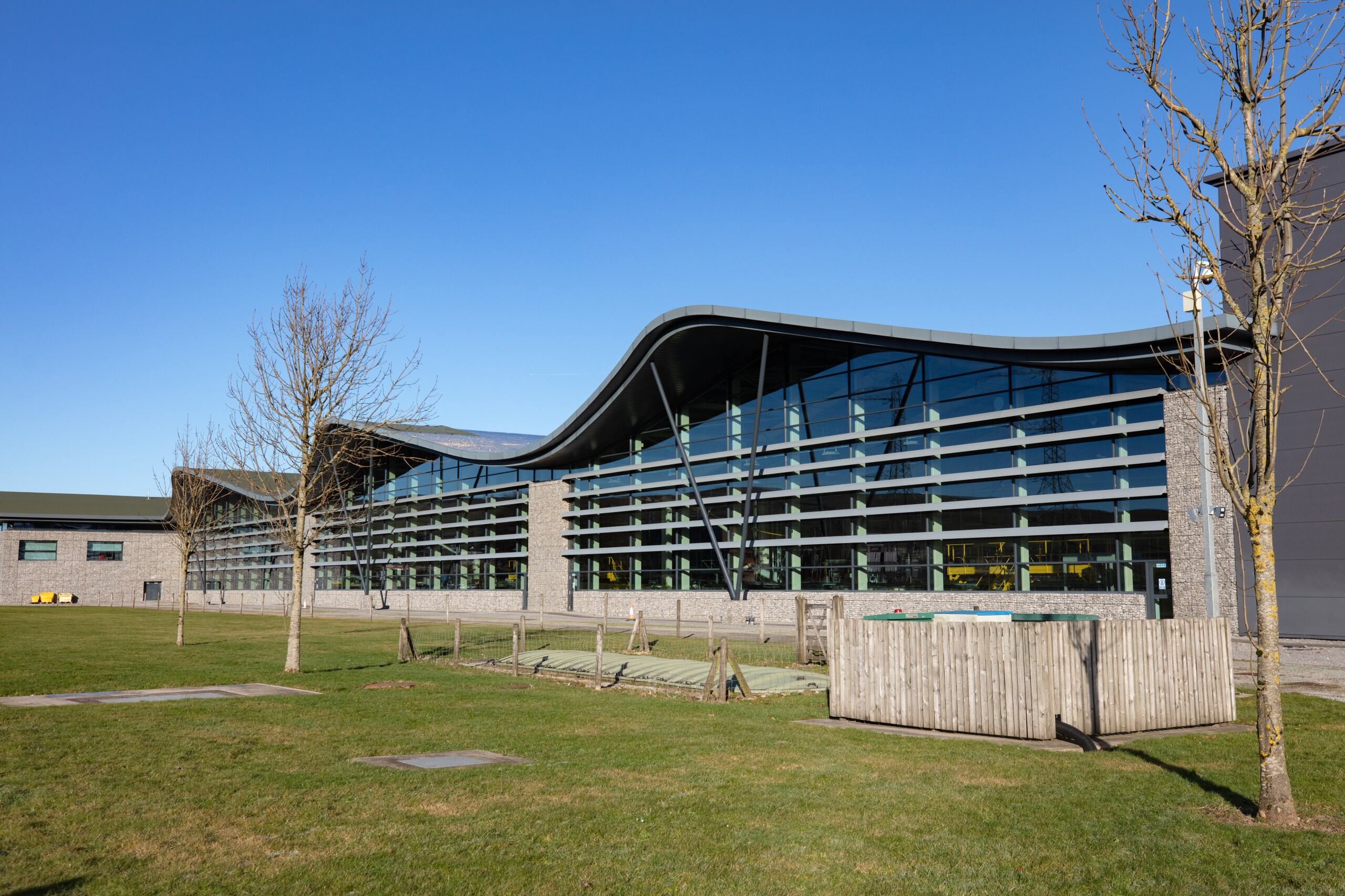 Buxton factory with glass front, green grass in front of it and blue sky in the back. 