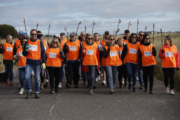 Group of 40 people wearing high vis vests and carrying litter pickers at the beach.
