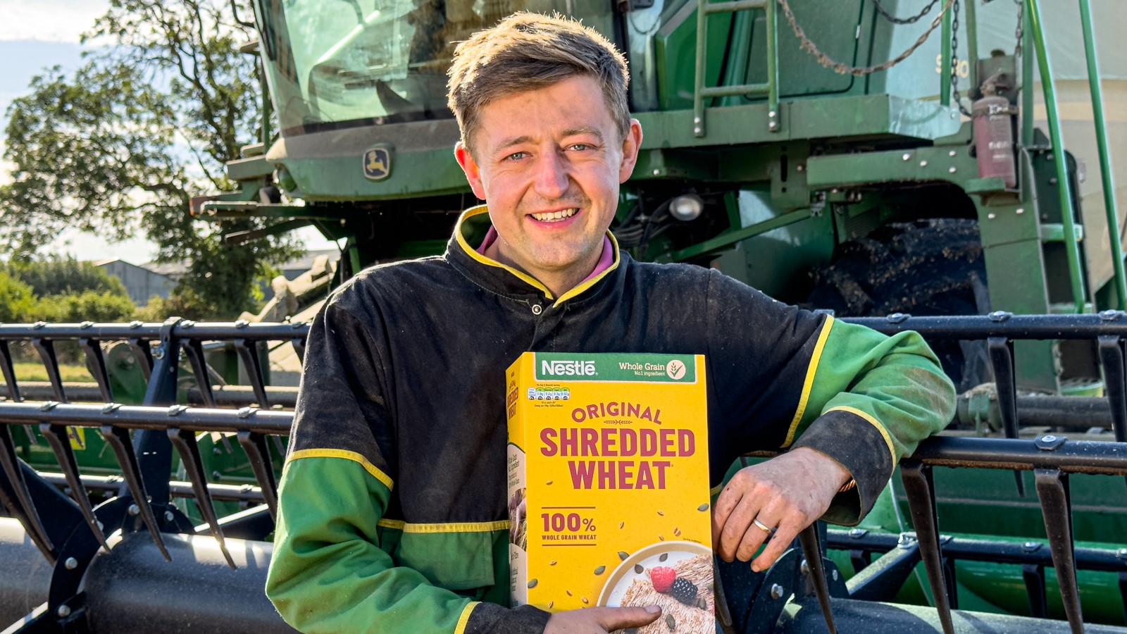 Male farmer standing in front of a combine harvester whilst holding a box of Shredded Wheat.