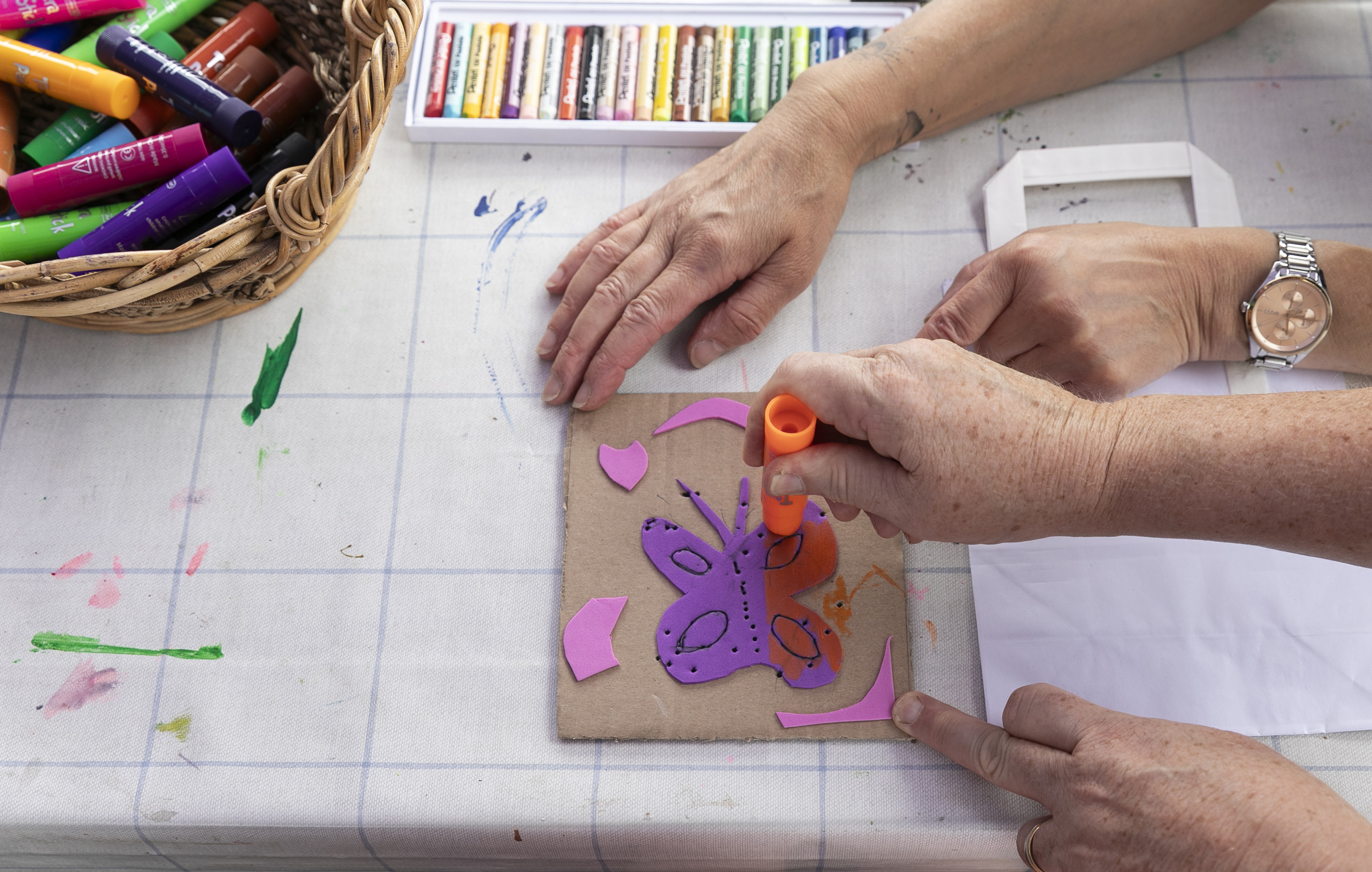 Two pair of hands colouring in a butterfly on cardboard