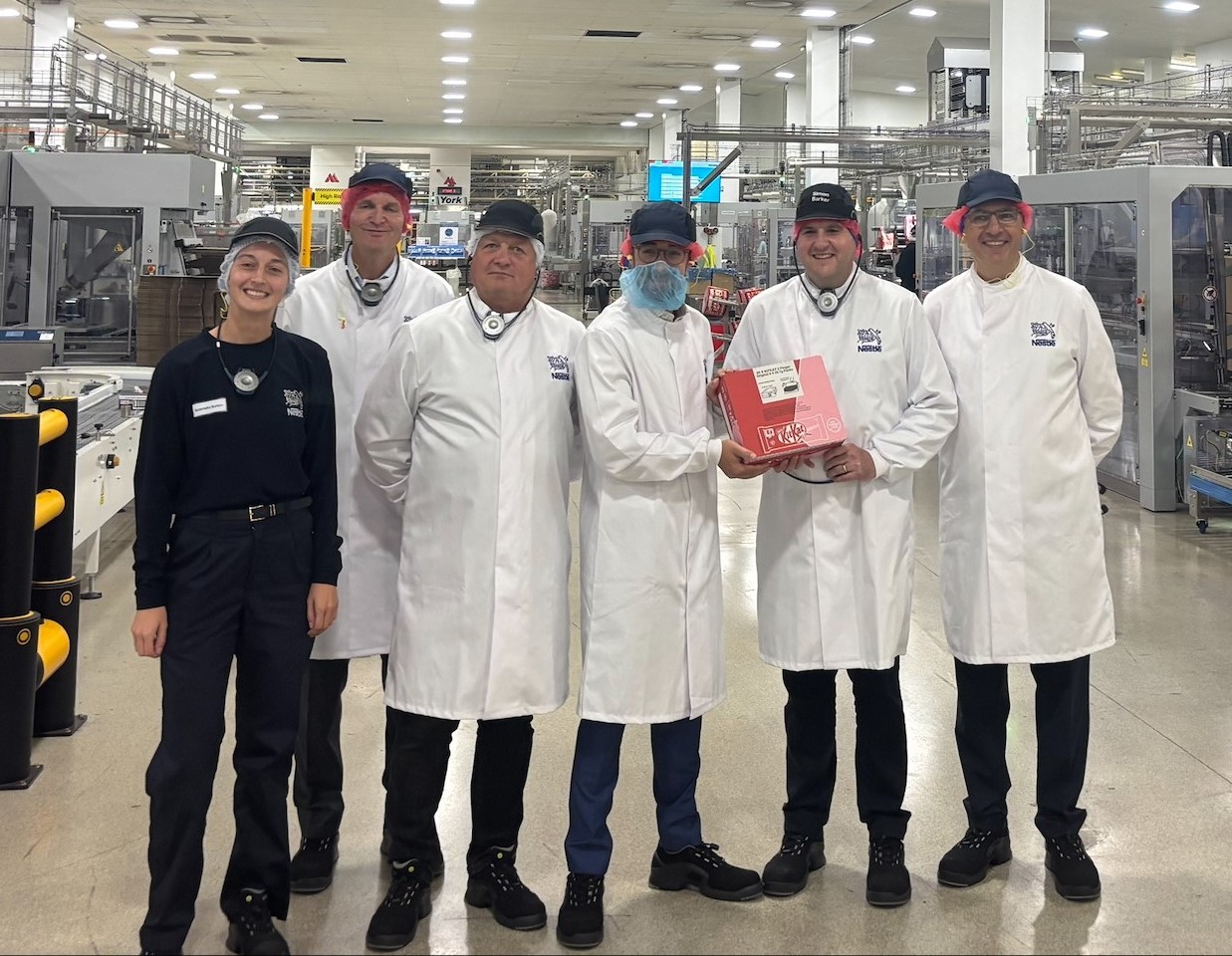 Luke Charters MP (centre) stood inside Nestlé York's KitKat factory, next to Nestlé employees, smiling.