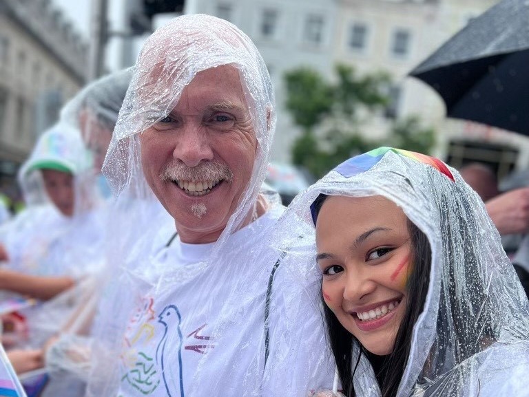 A man and a woman wearing rain ponchos whilst at a Pride march.