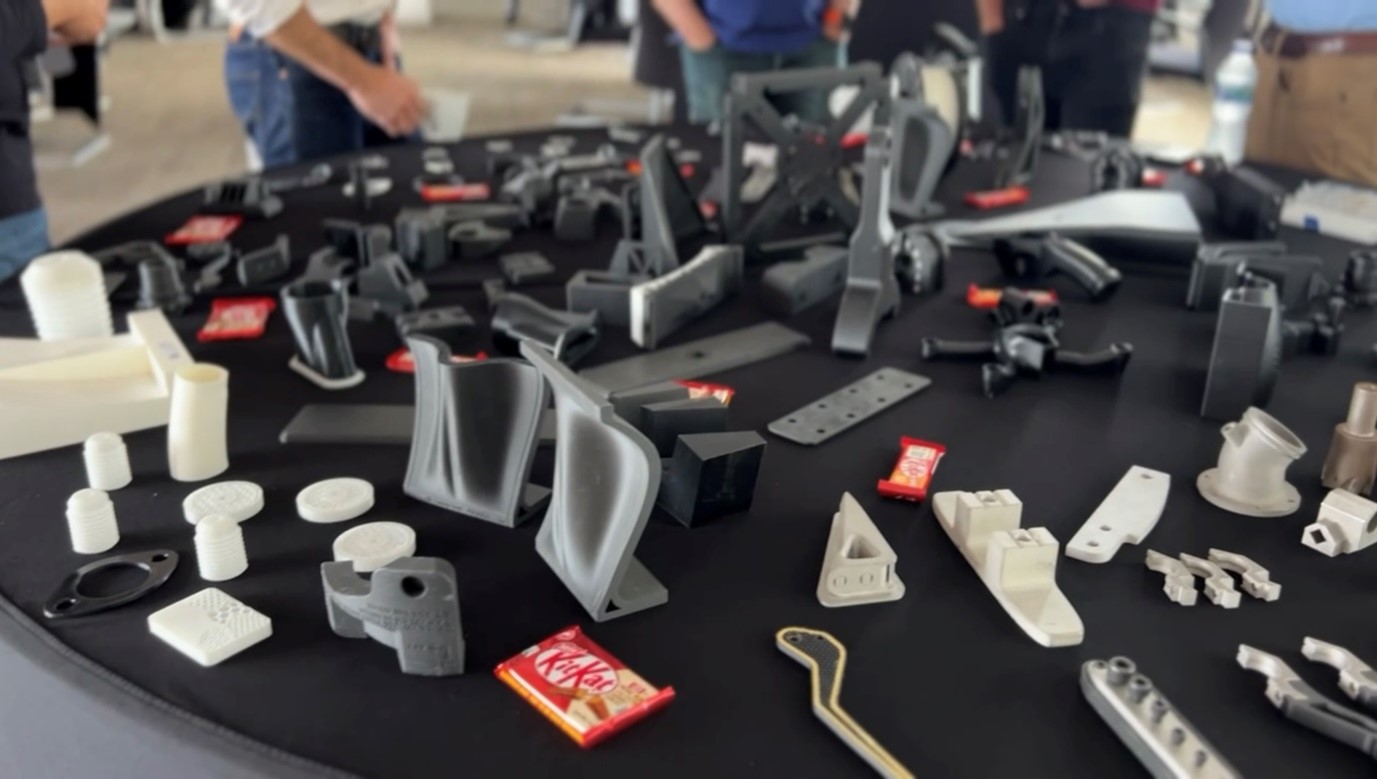 A landscape image of a black table with a variety of 3D printed machinery parts on it. KitKat bars are also seen on the table