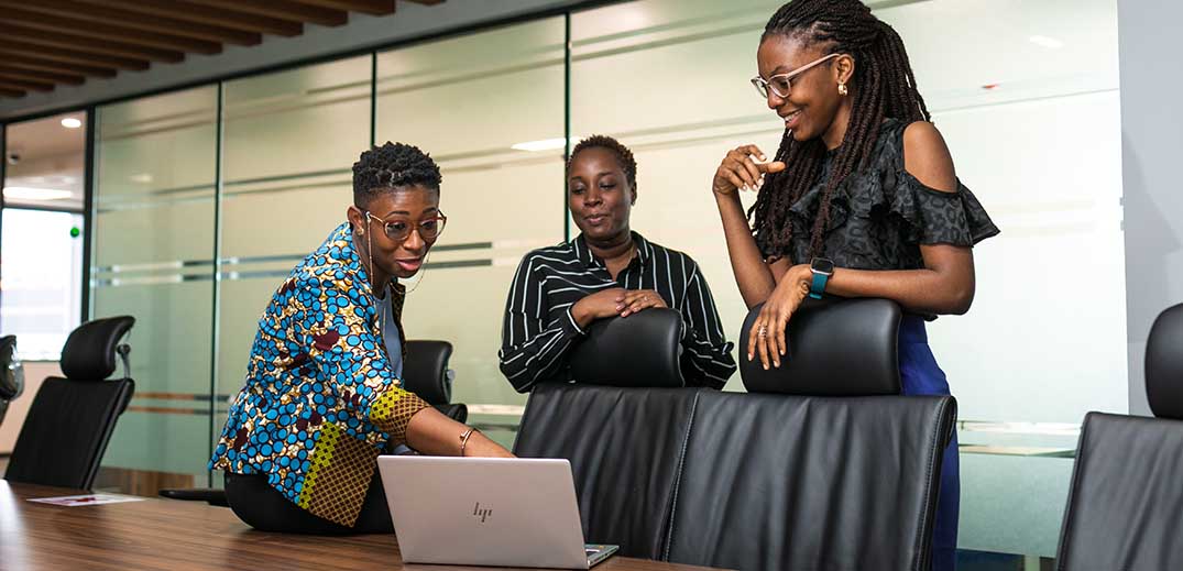 Three people in a conference room looking at a laptop on the table