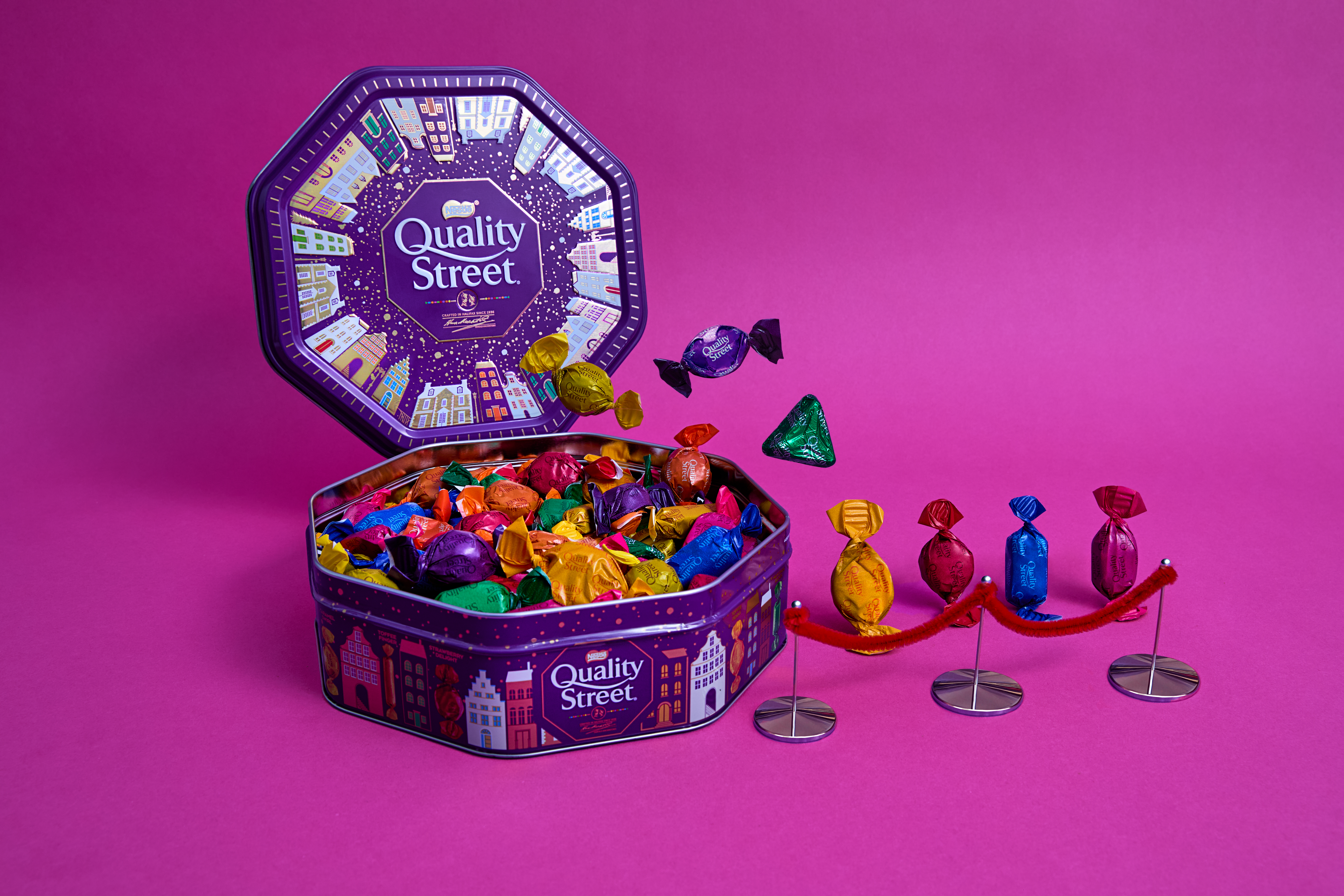 Quality Street tin with sweets in and other sweets lining up to get in