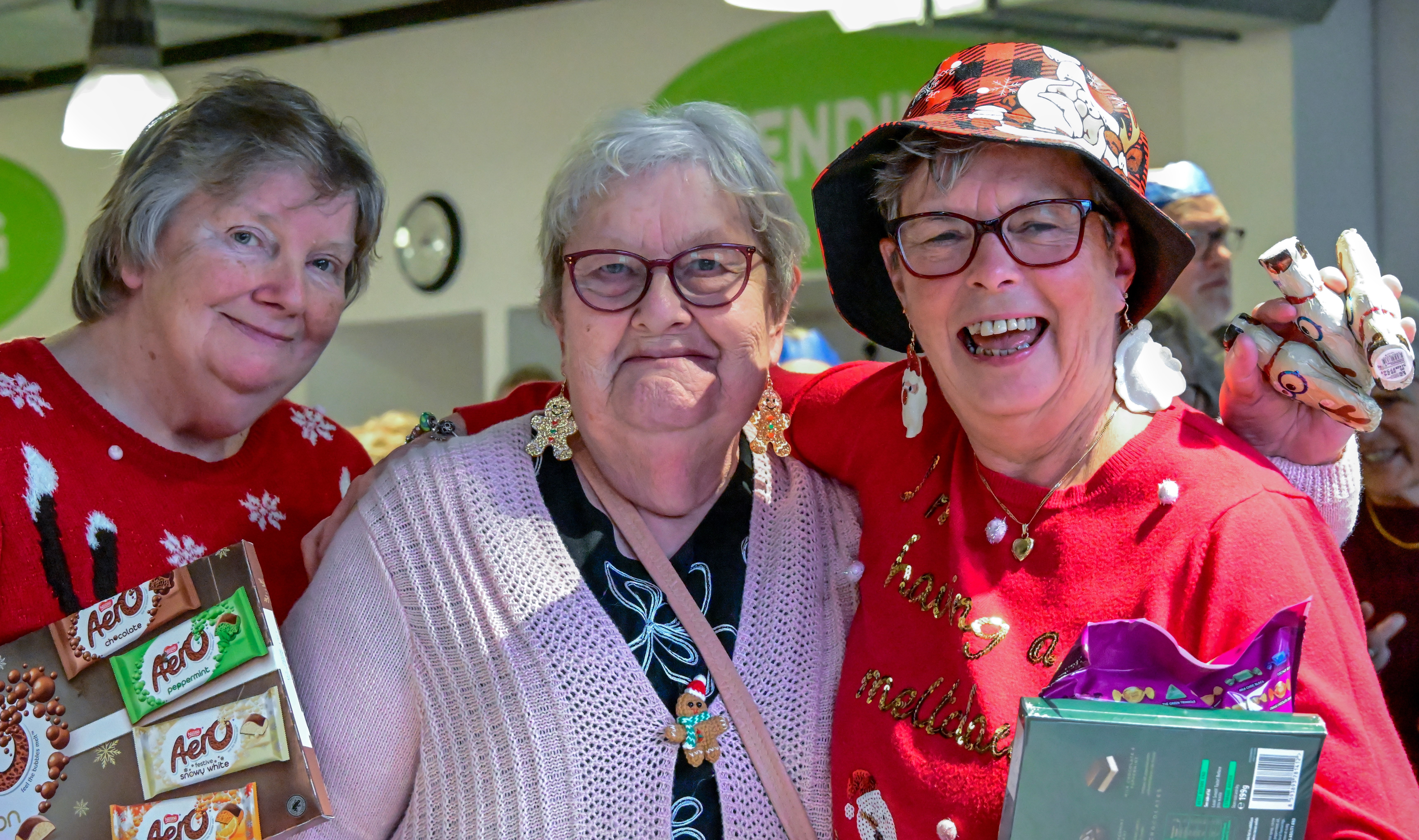 A landscape image of three Tutbury residents, smiling wearing festive jumpers and hats. 