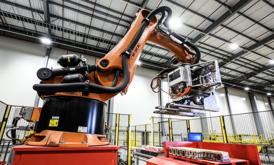 A landscape image of an orange RowPaq arm-grabber machine in a large distribution centre. 