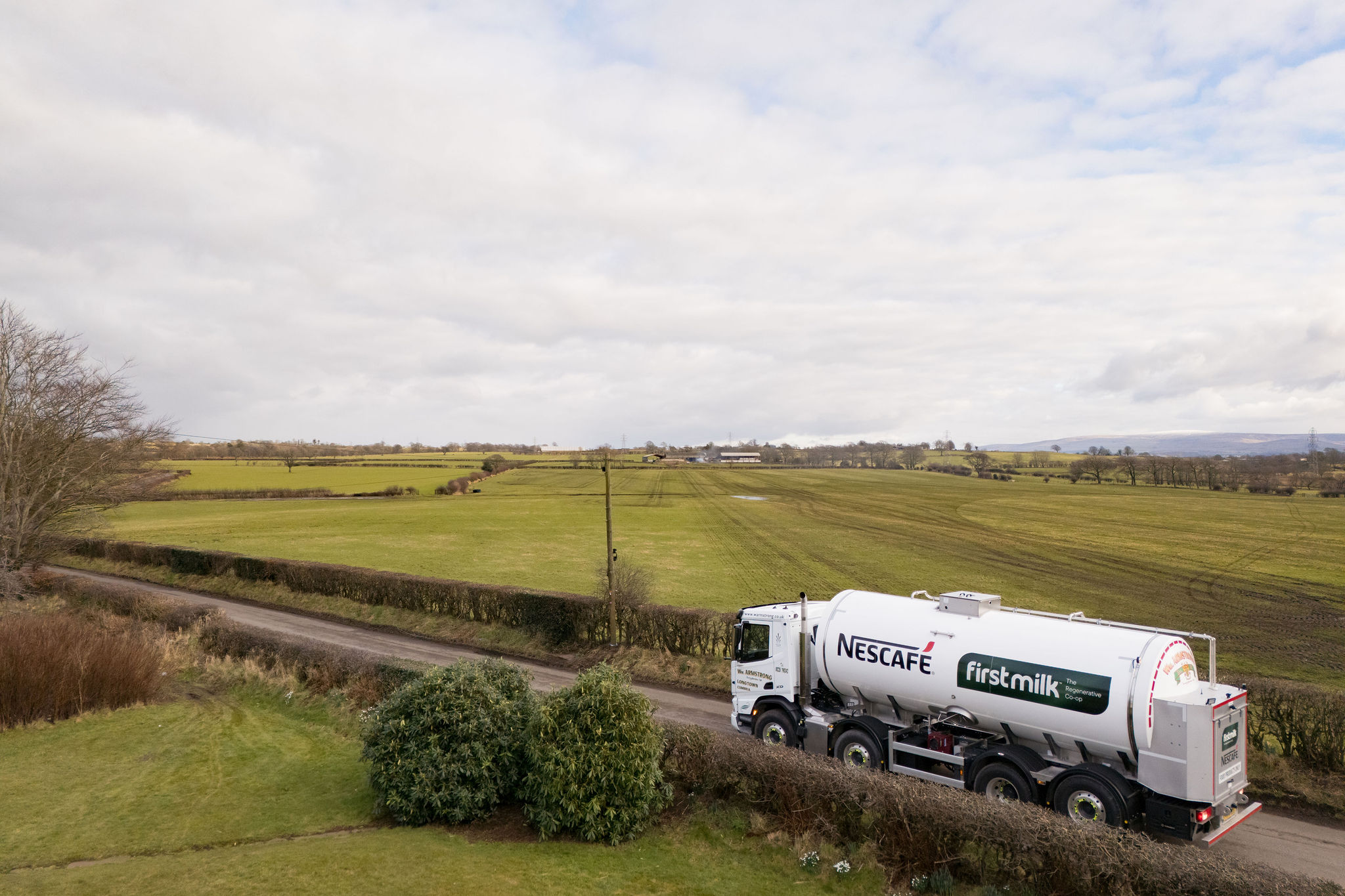A landscape image of a large white milk tanker, branded with a Nescafé and First Milk logo. 