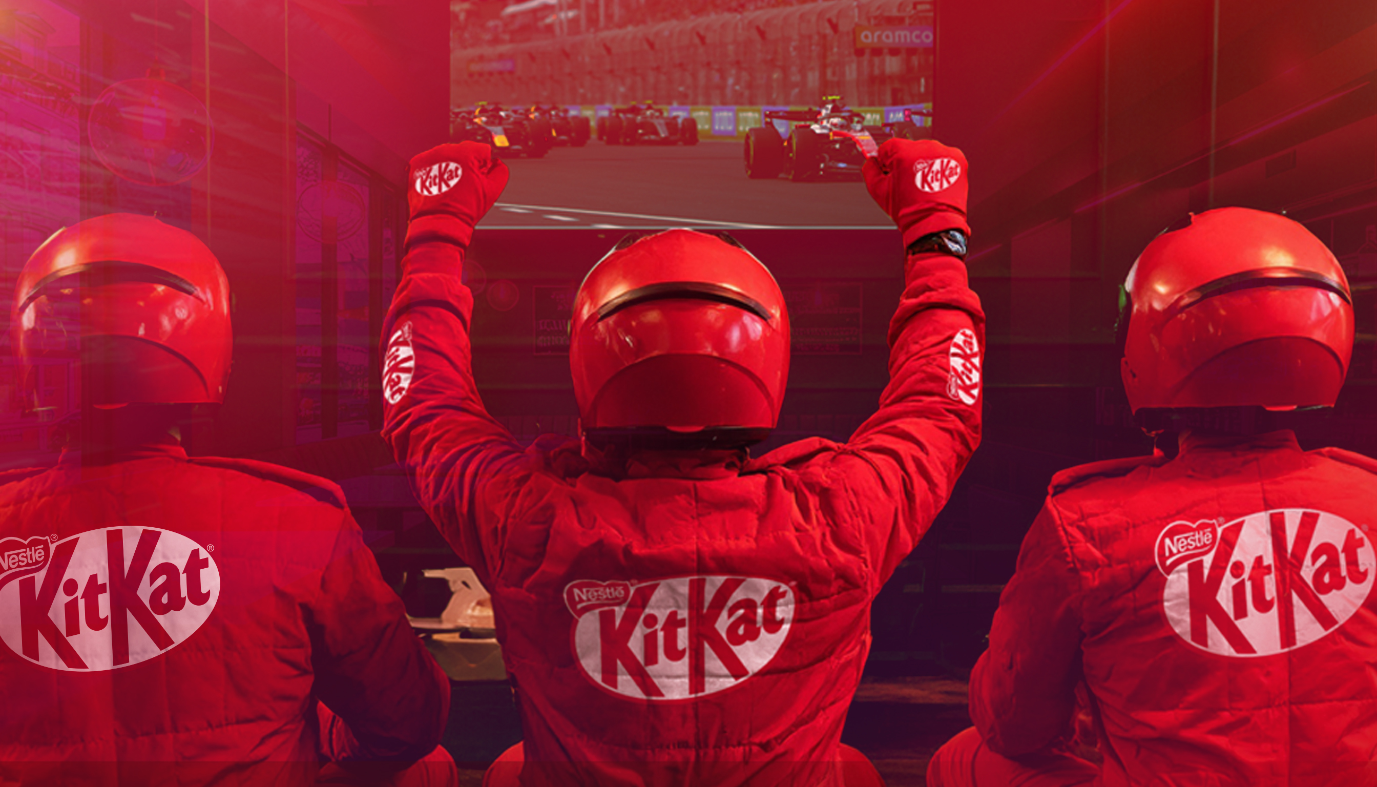 Three people dressed in KitKat overalls and a red helmet facing a TV screen which displays racing.