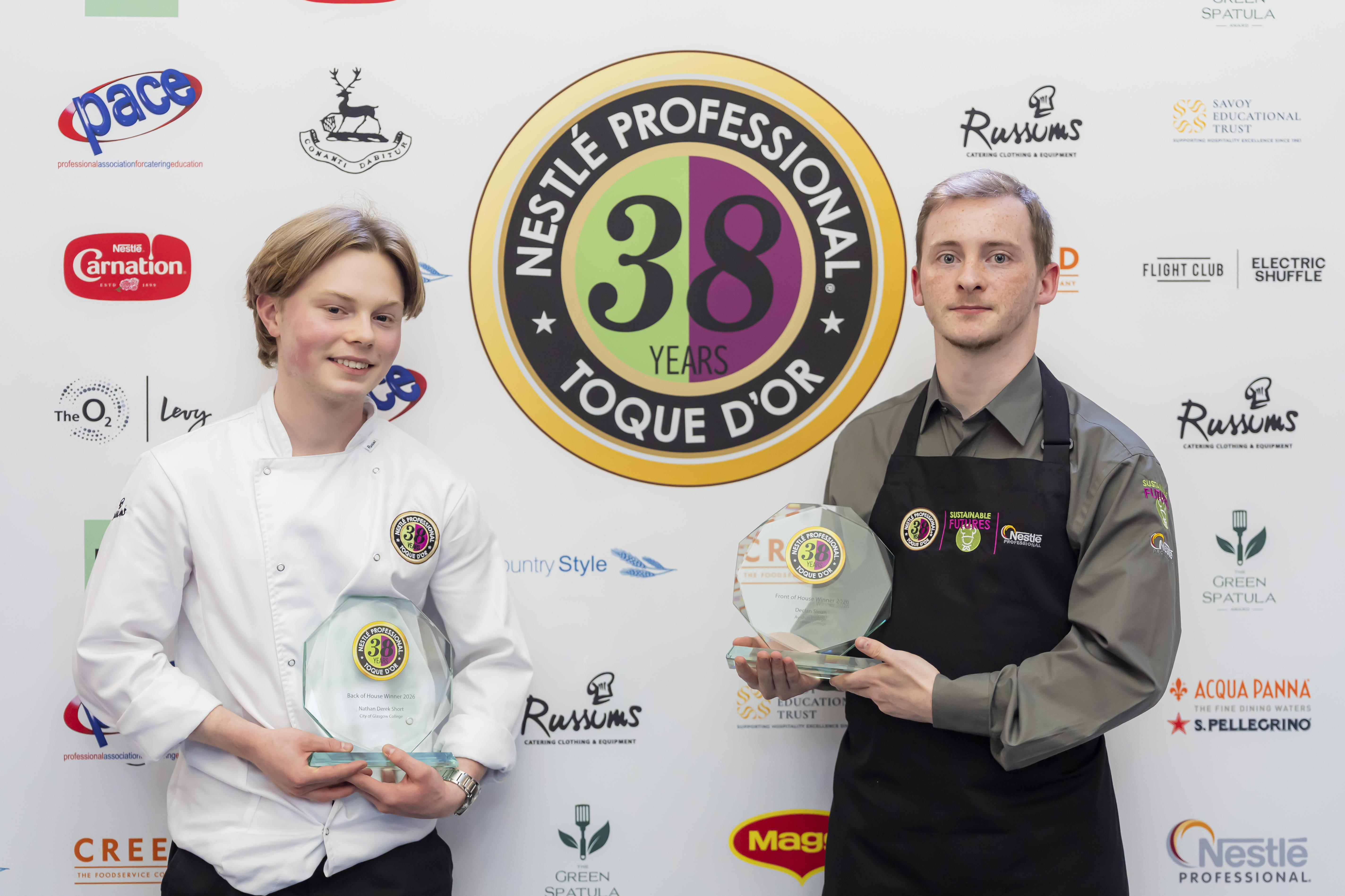 Two winners holding glass awards in front of a Nestlé Professional Toque d'Or branded wall.