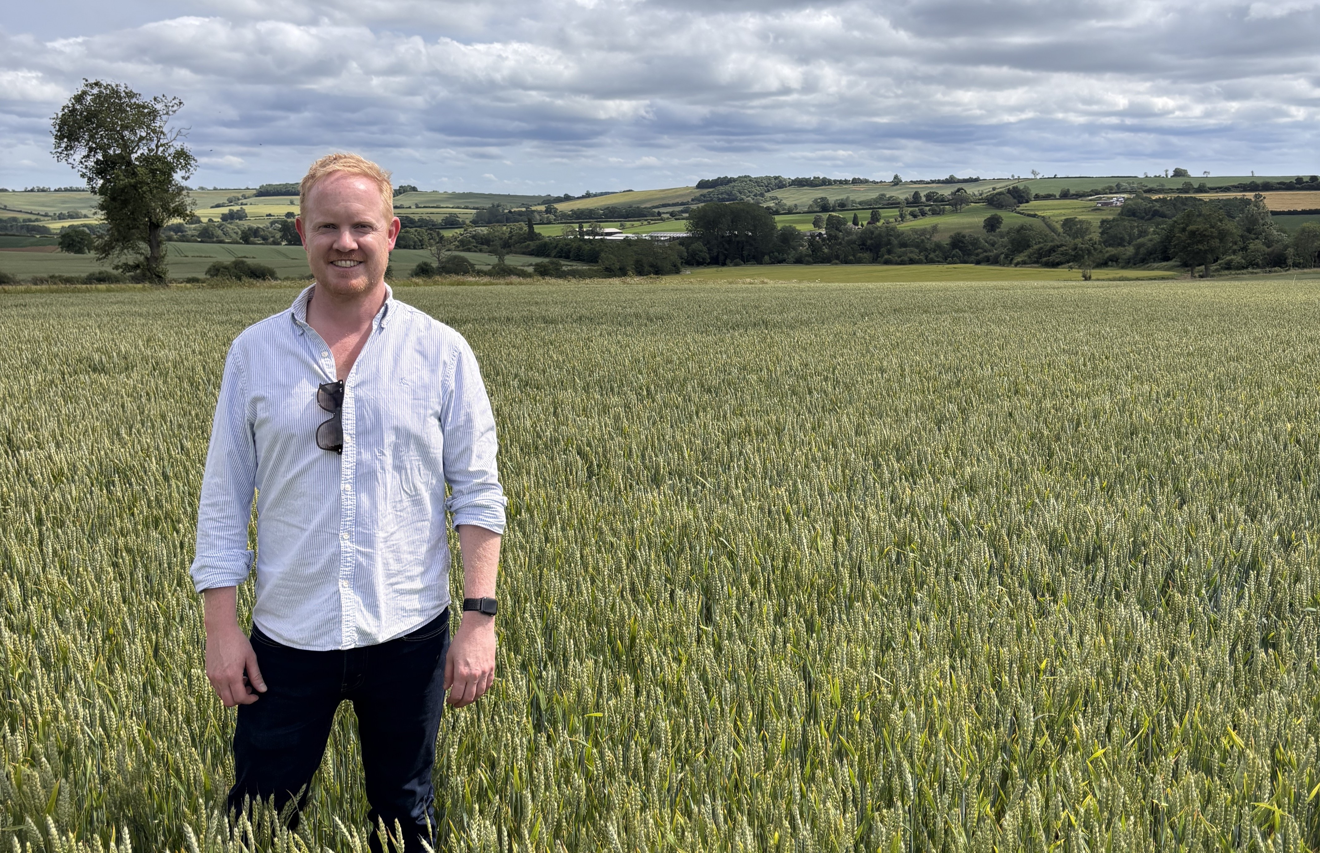 Man in white shirt and dark trousers standing in a field on a farm environment.