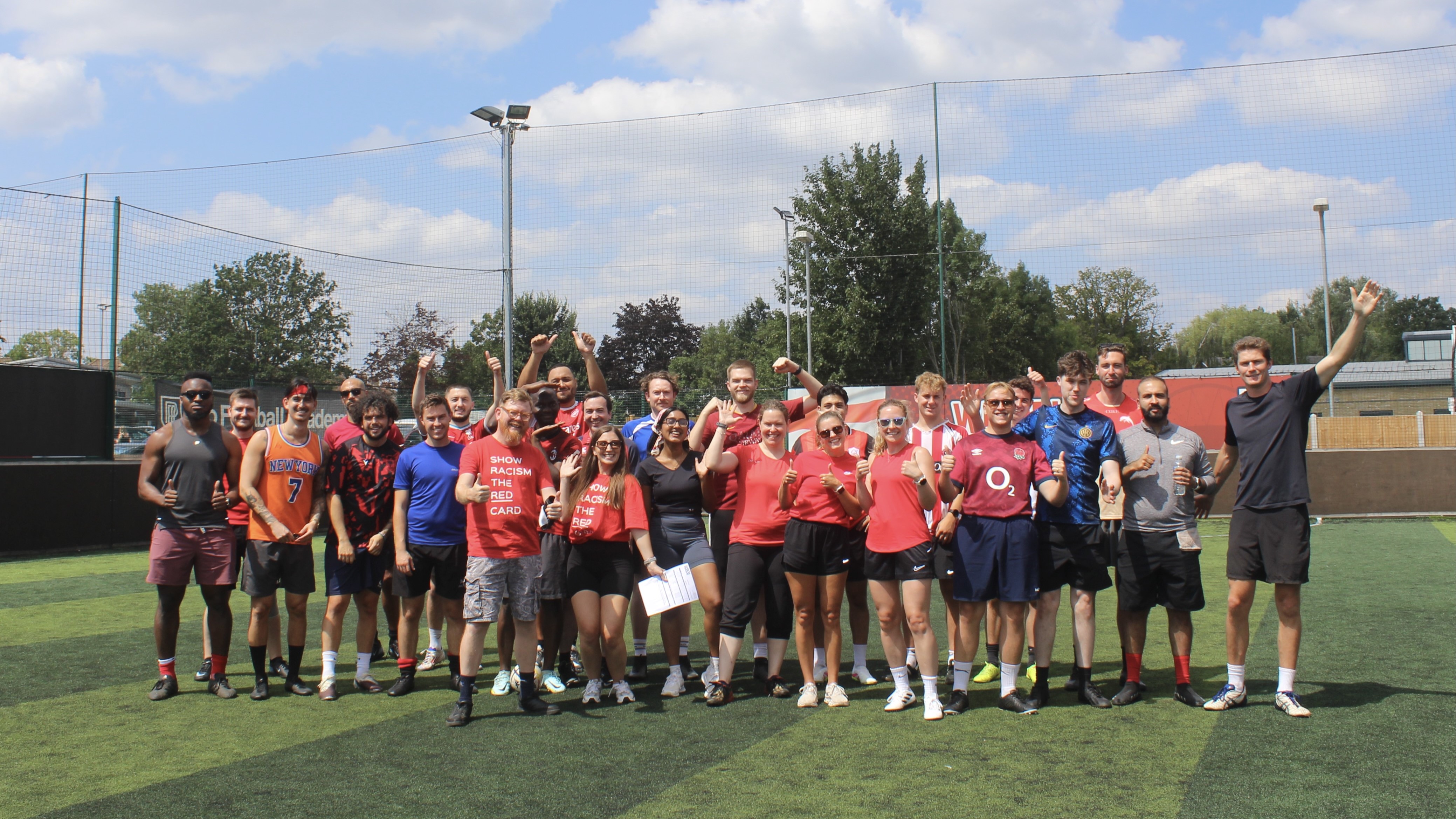 Group of around 25 colleagues wearing fitness clothes posing for a group photo in a football field.