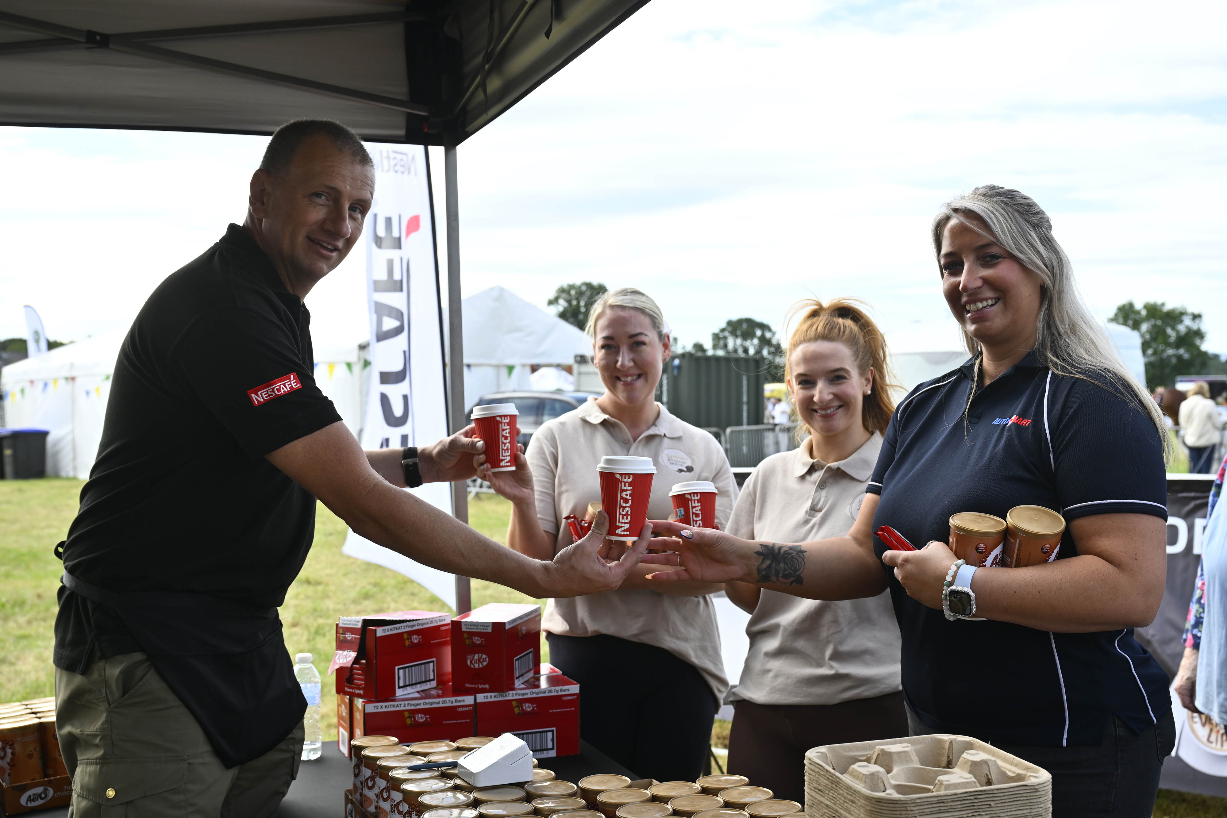 A landscape image of a group of Nescafé employees in black polo tops with red Nescafé writing on the sleeve, holding coffee.