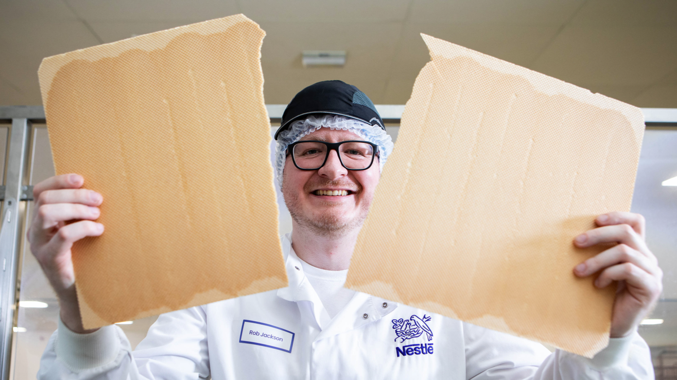 Man wearing glasses holding up two sheets of wafer in each hand.