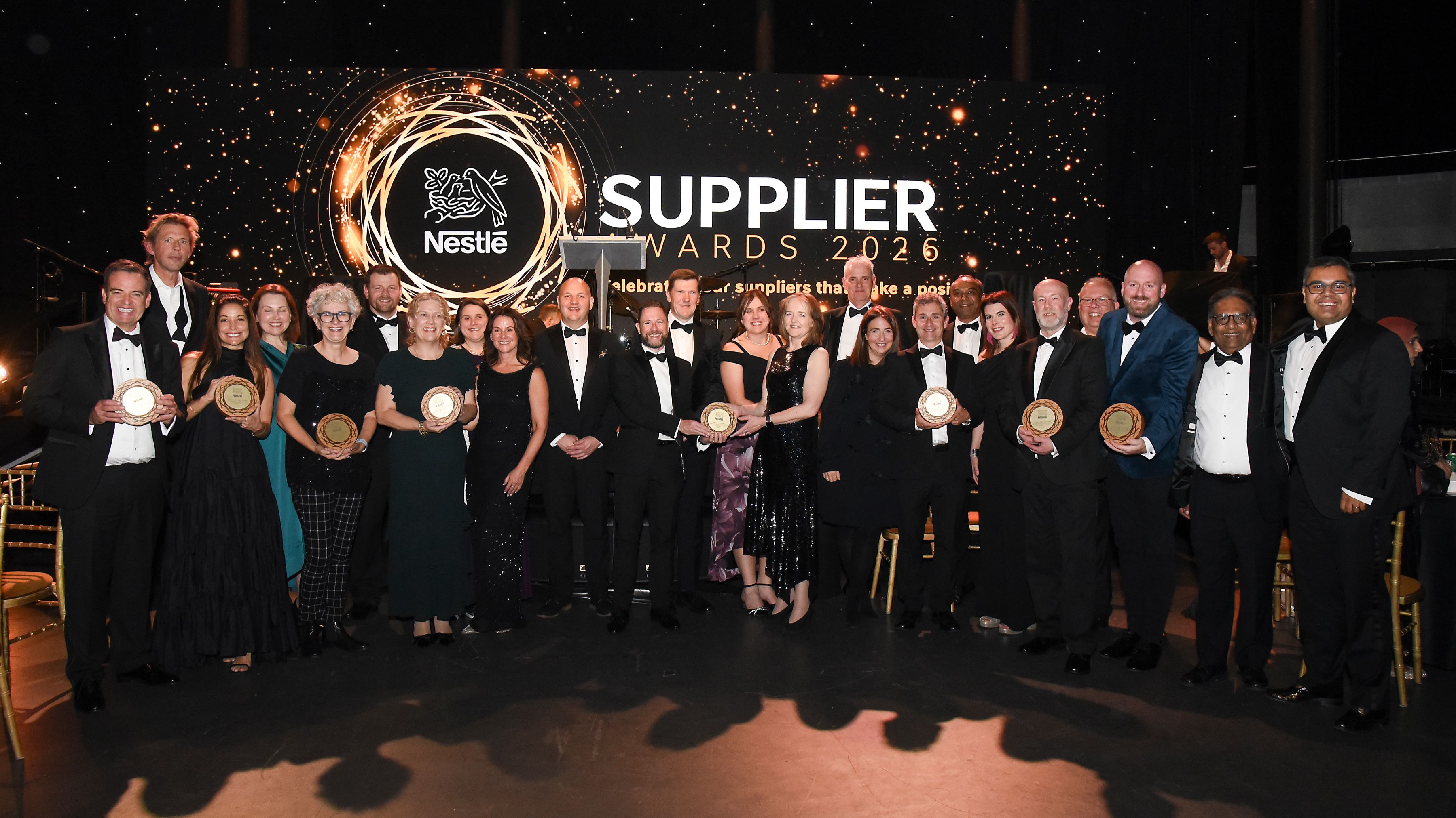 More than 20 people dressed in evening wear gathered in front of a stage decorated for the Nestlé Supplier Awards.