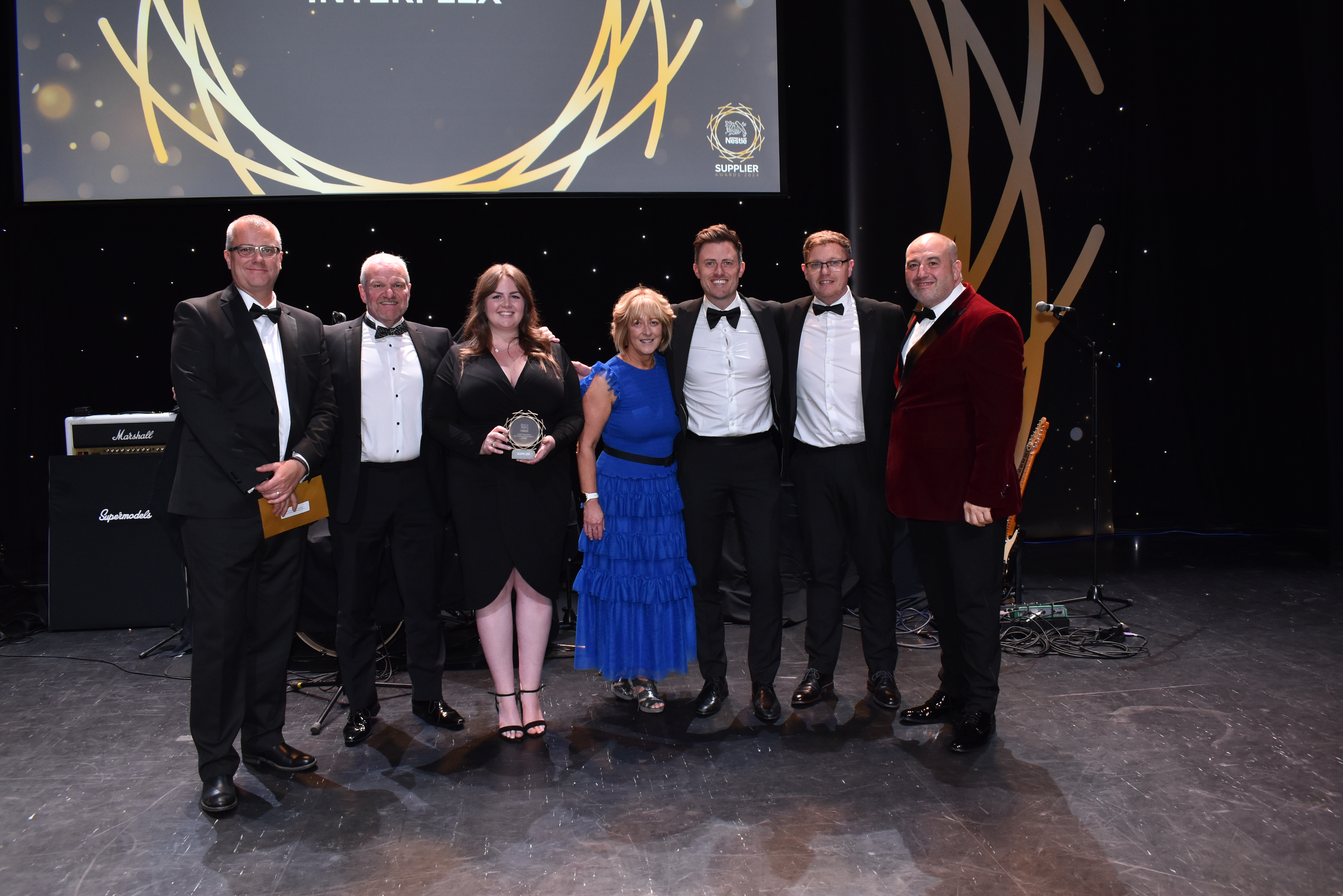 Seven people on stage and surrounding an award.