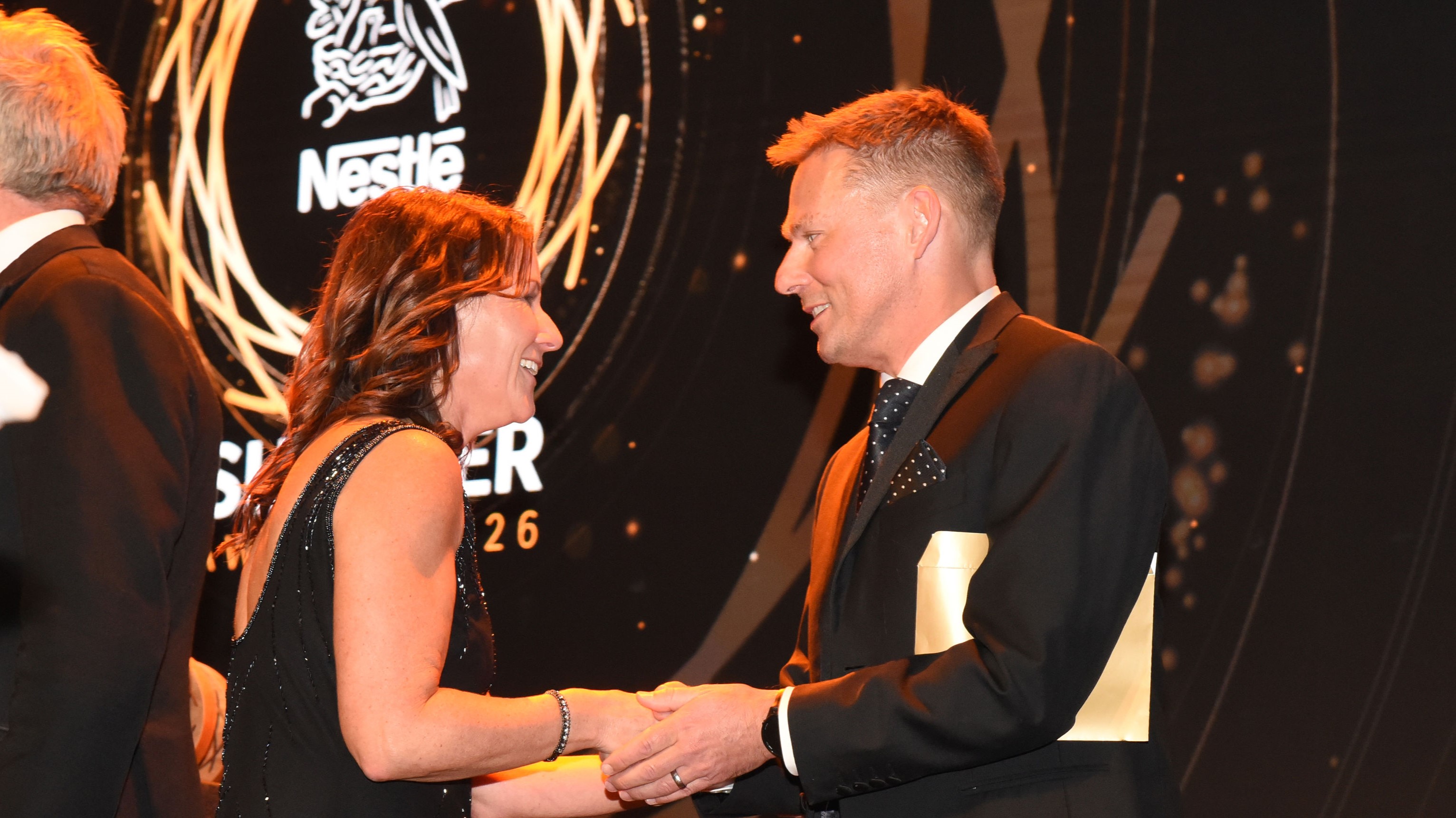 A woman and a man congratulating another whilst stood on stage.