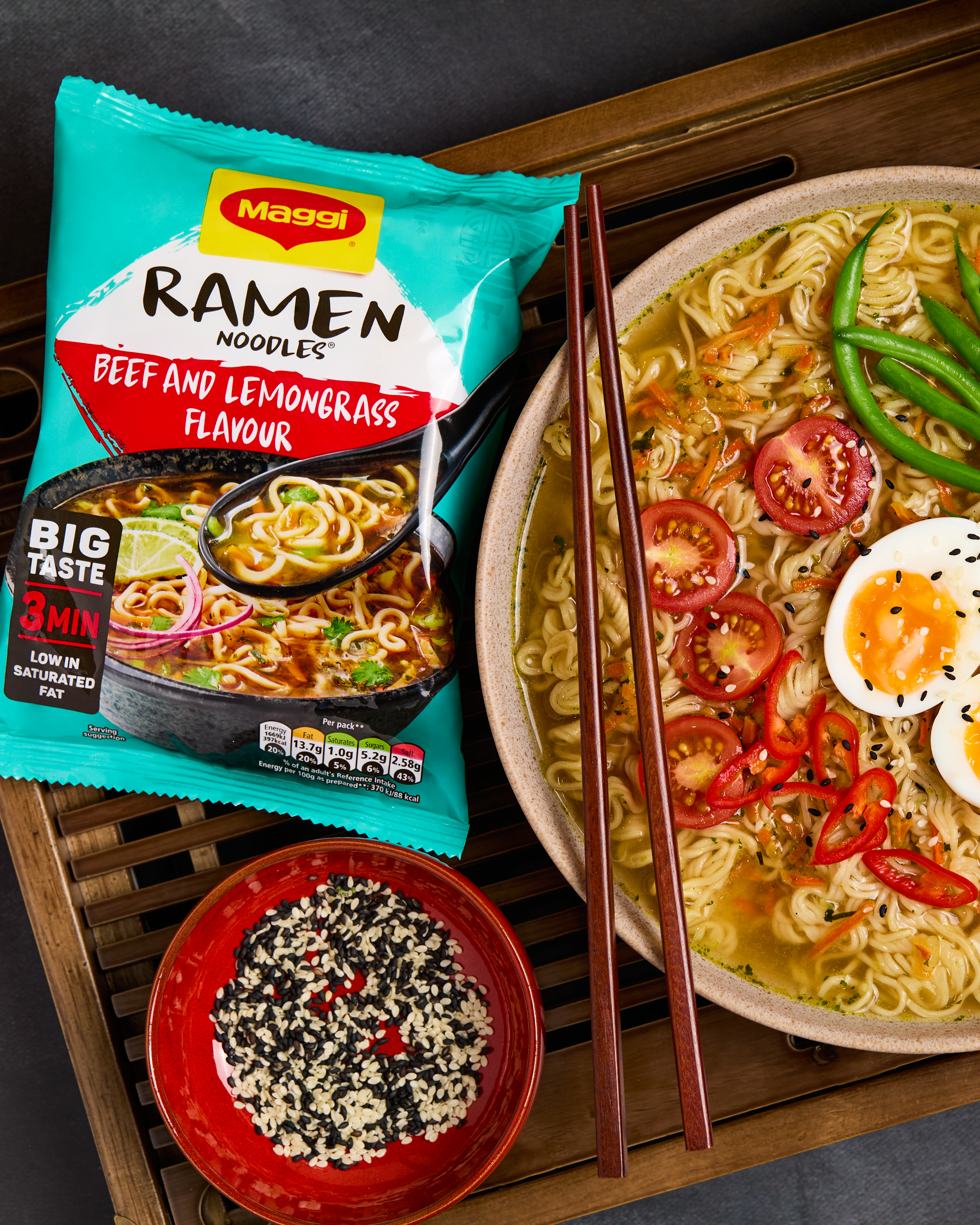 Packet of Beef & Lemongrass Maggi Ramen next to a bowl of noodles and chopsticks, sitting on a wooden surface.