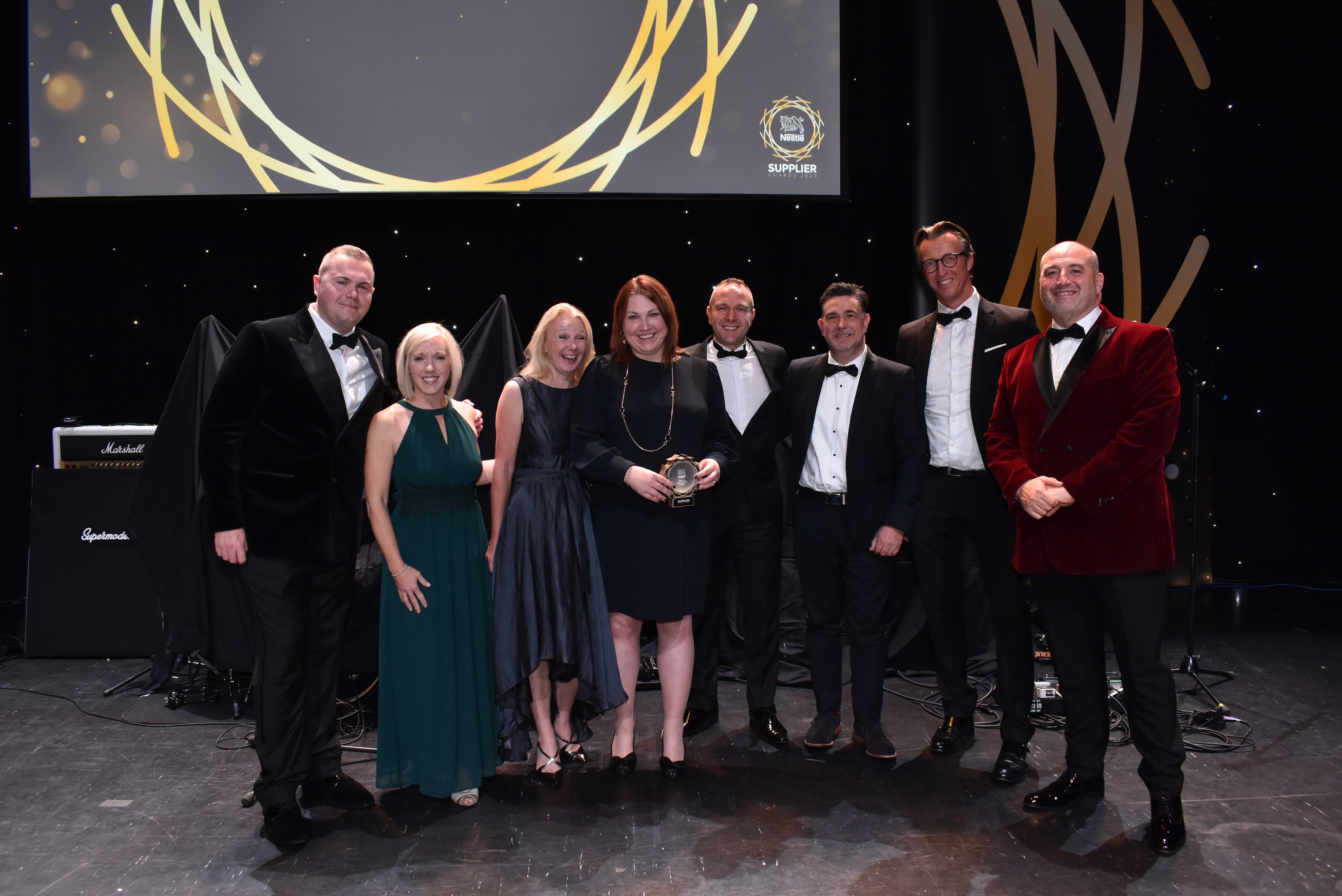Eight people on stage and surrounding an award.