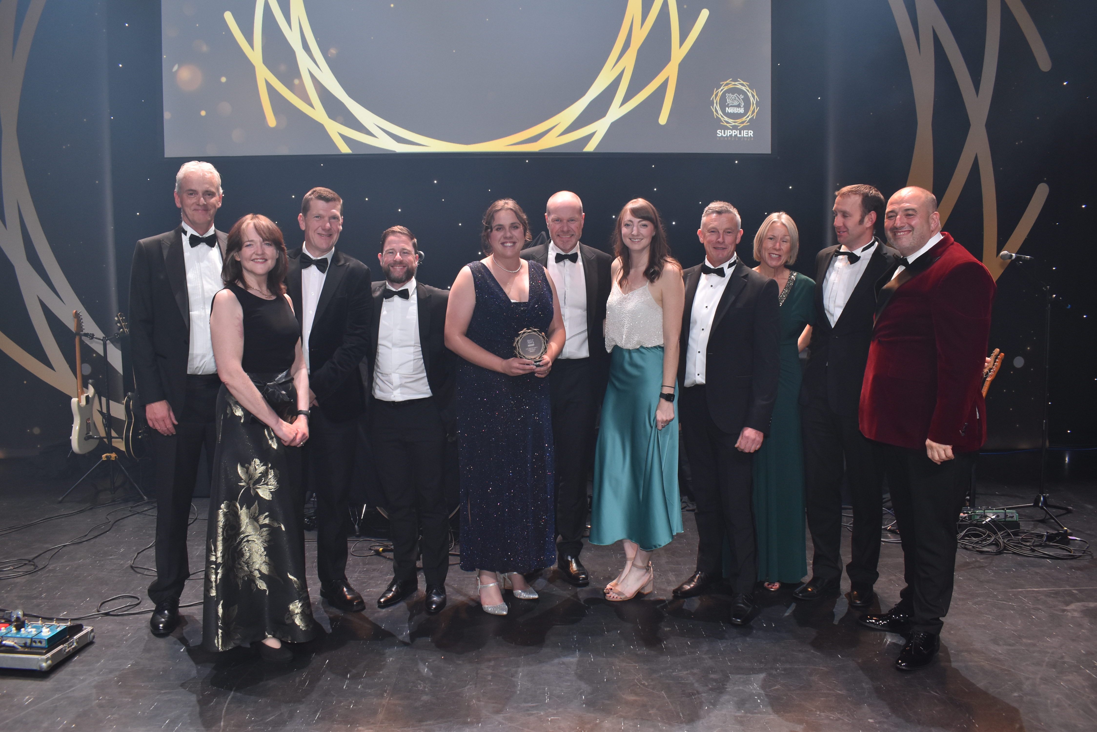 Eleven people on stage and surrounding an award.