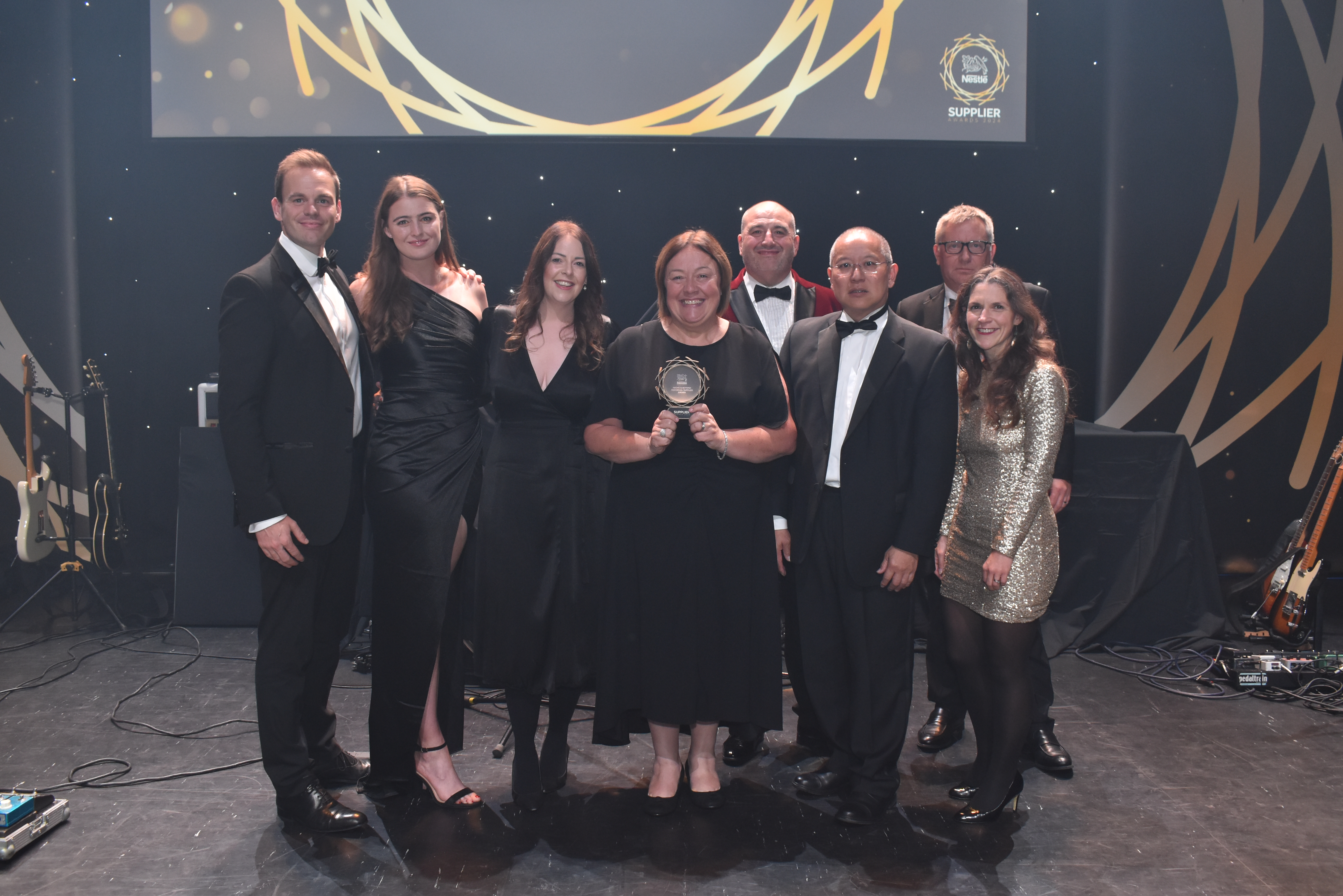 Eight people on stage and surrounding an award.