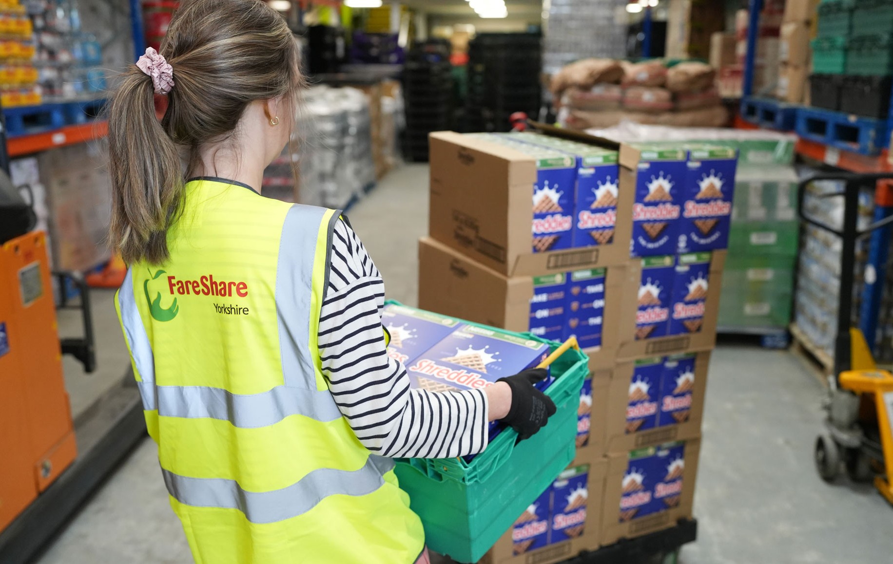 A landscape image of a female FareShare worker in a high-vis delivering pallets of Shreddies cereal in a Nestlé warehouse.