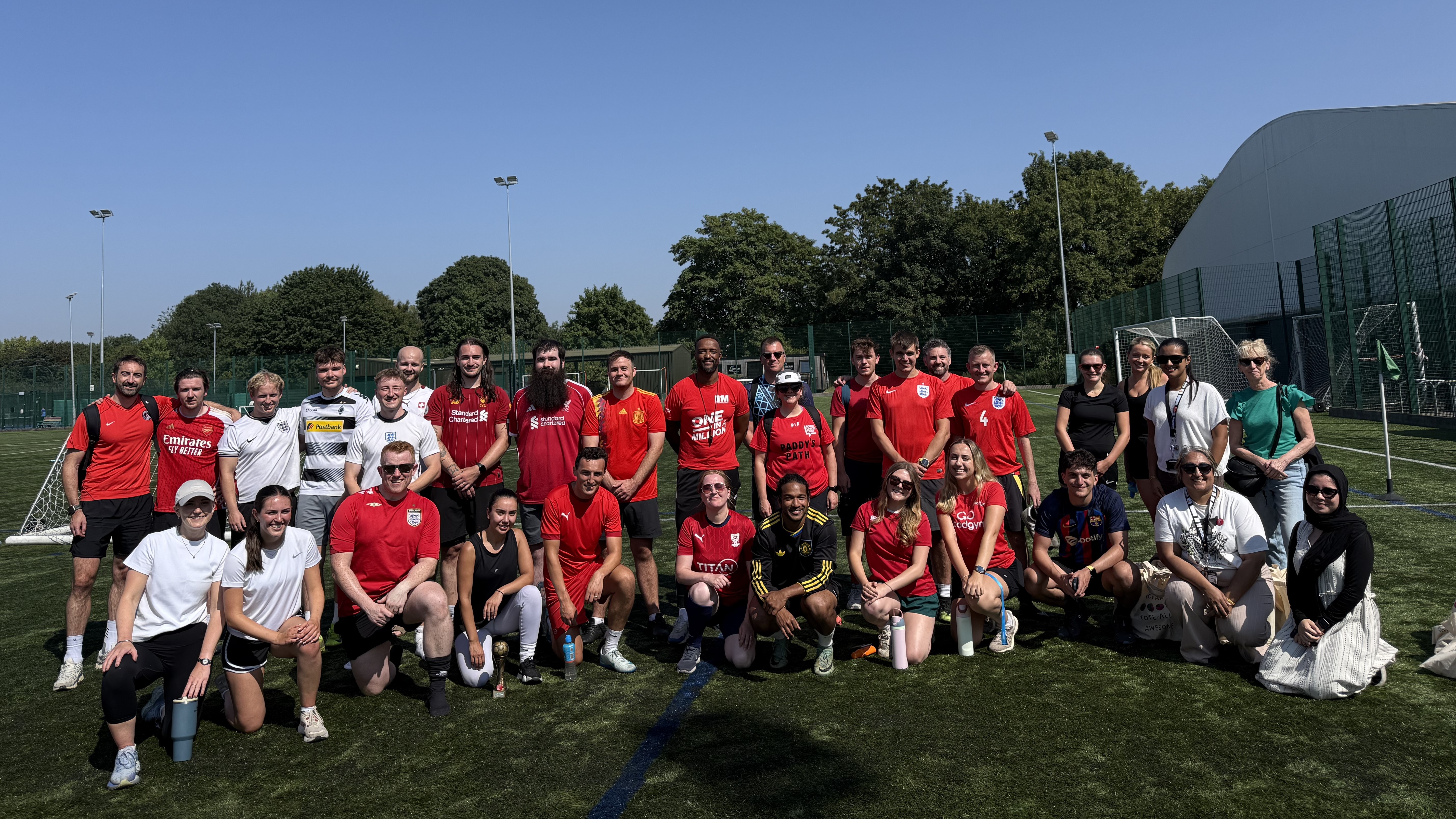 Group of around 30 colleagues gathered for a group photo in a football field.