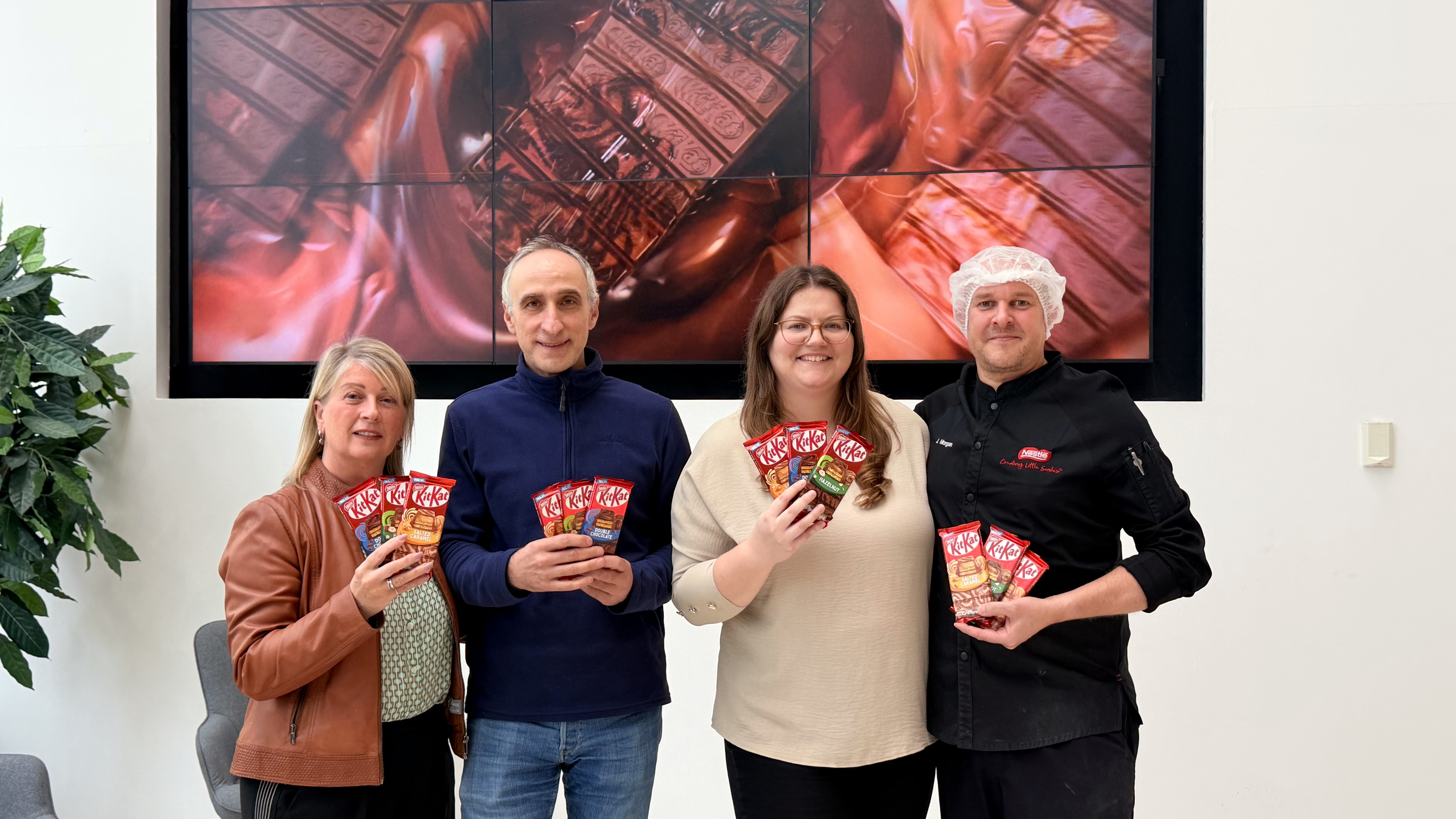 Group of four people standing together and all holding KitKat sharing bars.