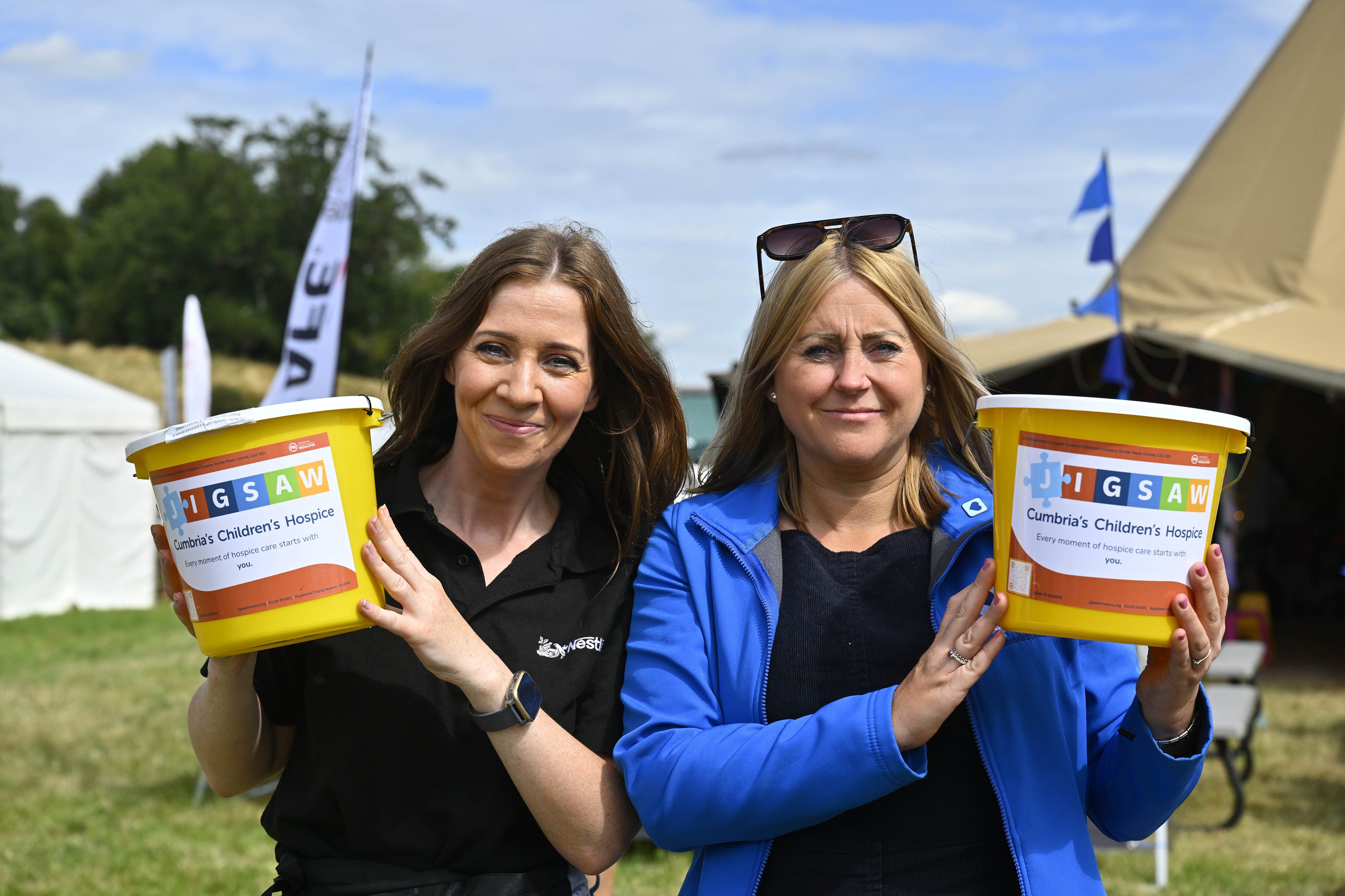 A landscape image of two Dalston employees, smiling, holding charity buckets for Eden Valley Hospice.