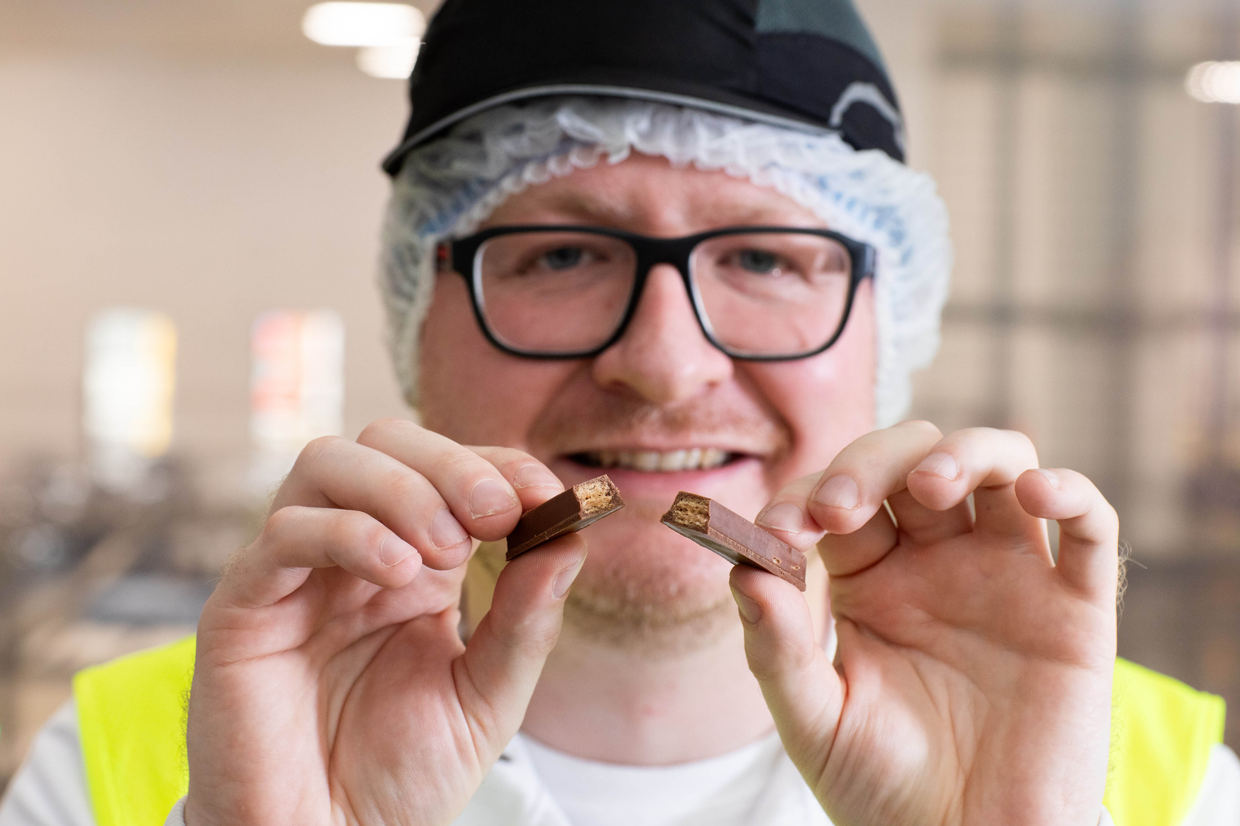 Man wearing glasses holding up a KitKat bar broken in half.