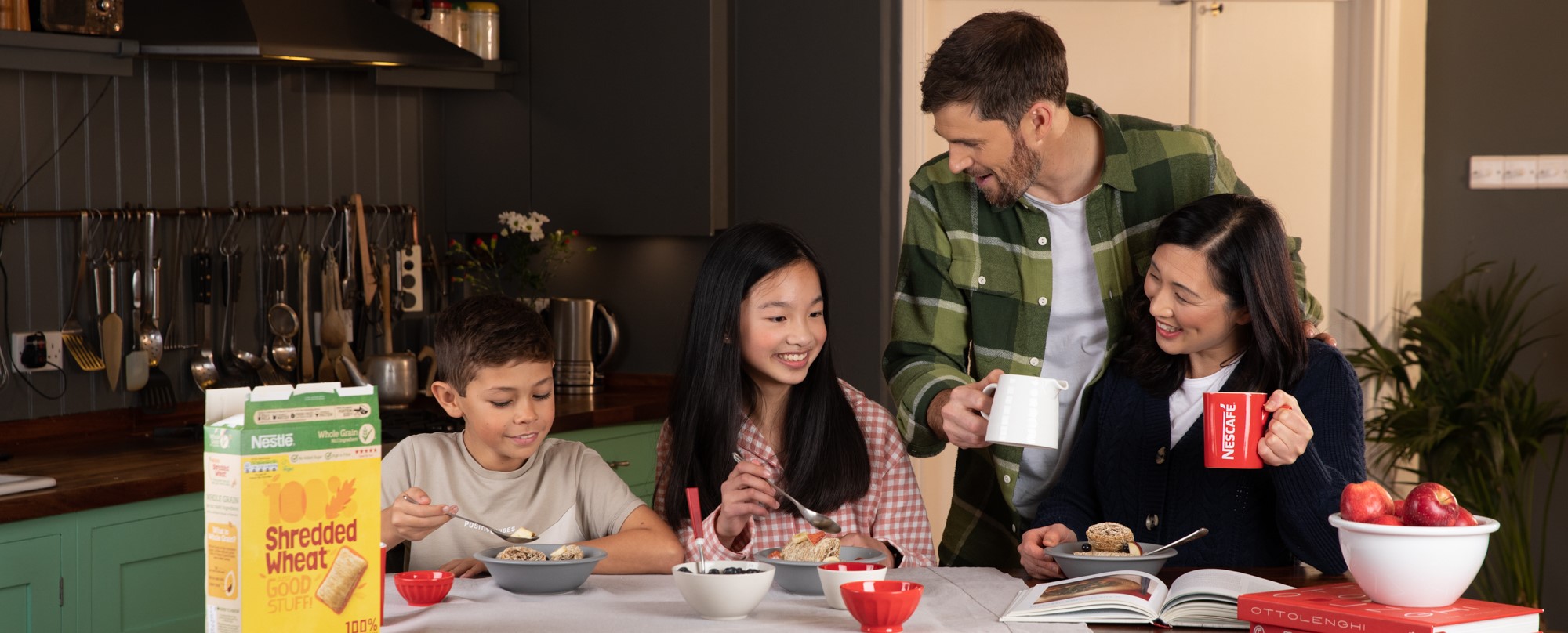 family of four sat around a breakfast table eating cereal and drinking coffee