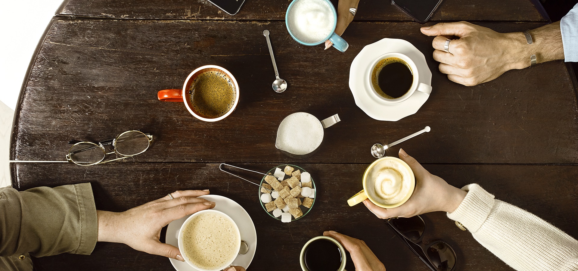 six different types of coffee on a table with people around the table holding the mugs