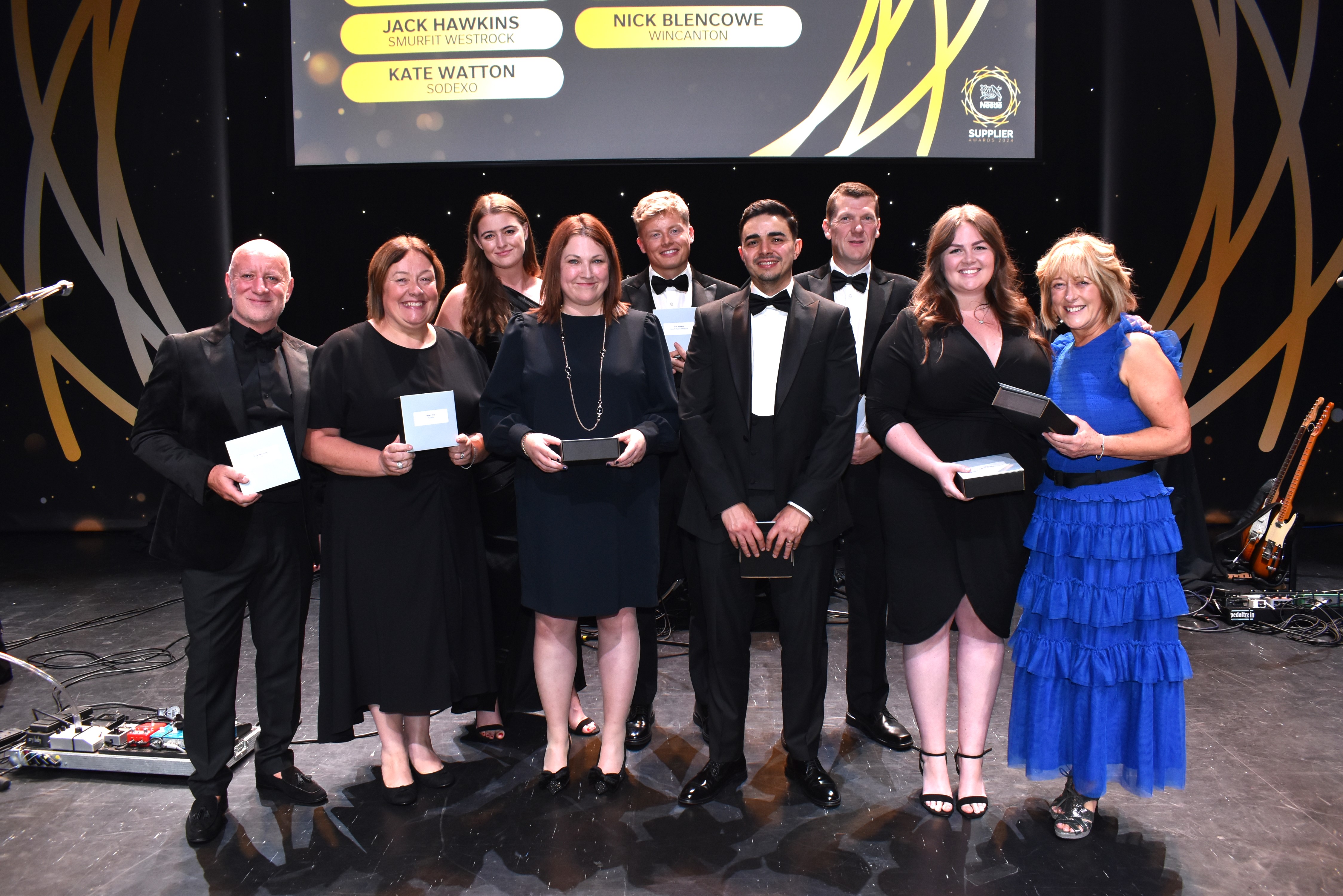Nine people on stage and surrounding an award