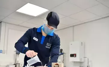 Nestlé employee pouring liquid into a container in a food production setting.
