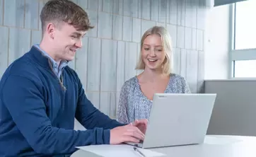 Two people working together on a laptop in an office.