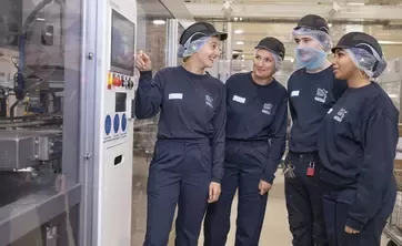 Four people standing beside machinery in a production facility