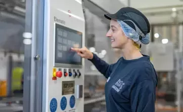 Apprentice operating a touchscreen control panel on manufacturing equipment in a food production facility while wearing workplace safety gear.