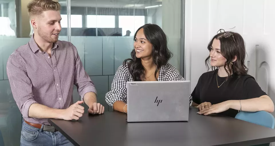 Two women and a man standing chatting behind a laptop