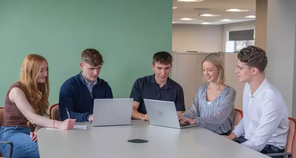Five colleagues working together around a table with laptops.