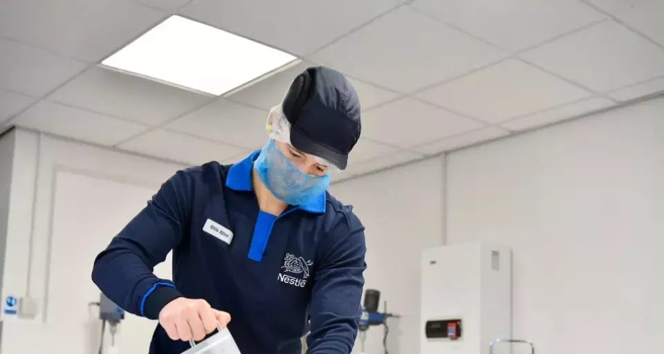 Nestlé employee pouring liquid into a container in a food production setting.
